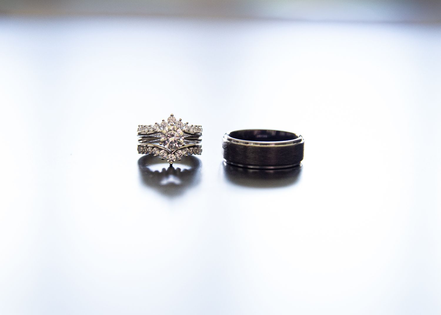 Wedding rings displayed on white surface showing diamond engagement ring and black band.