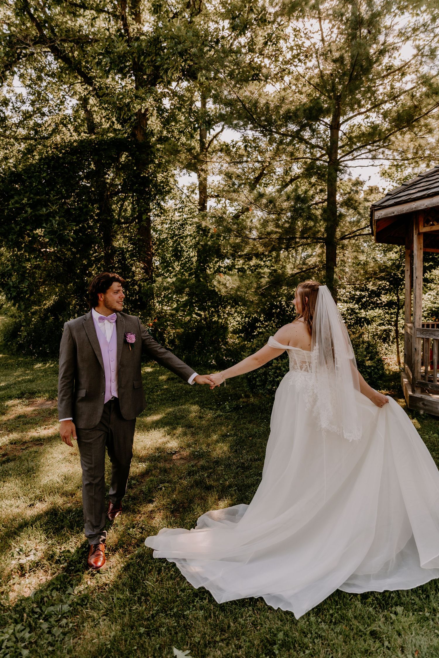 Bride and groom walk hand in hand through a lush green wooded garden path.