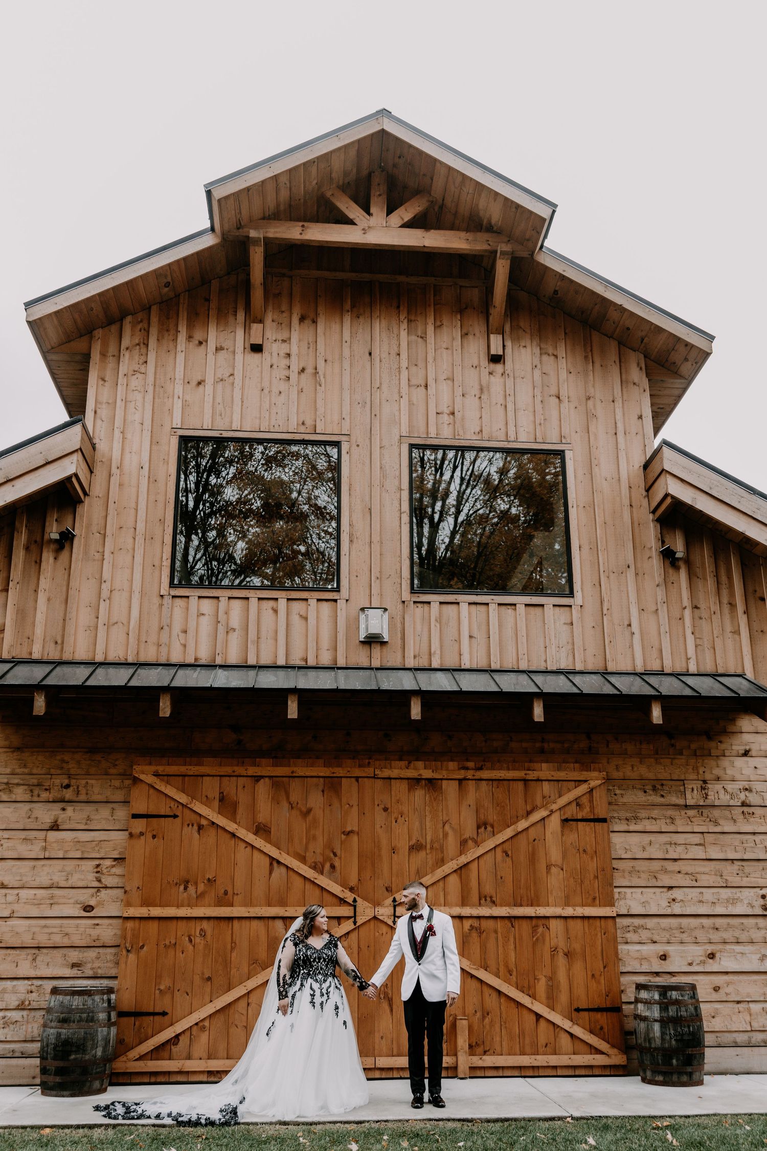 Rustic barn wedding venue with couple posing in front of large wooden doors at sunset.