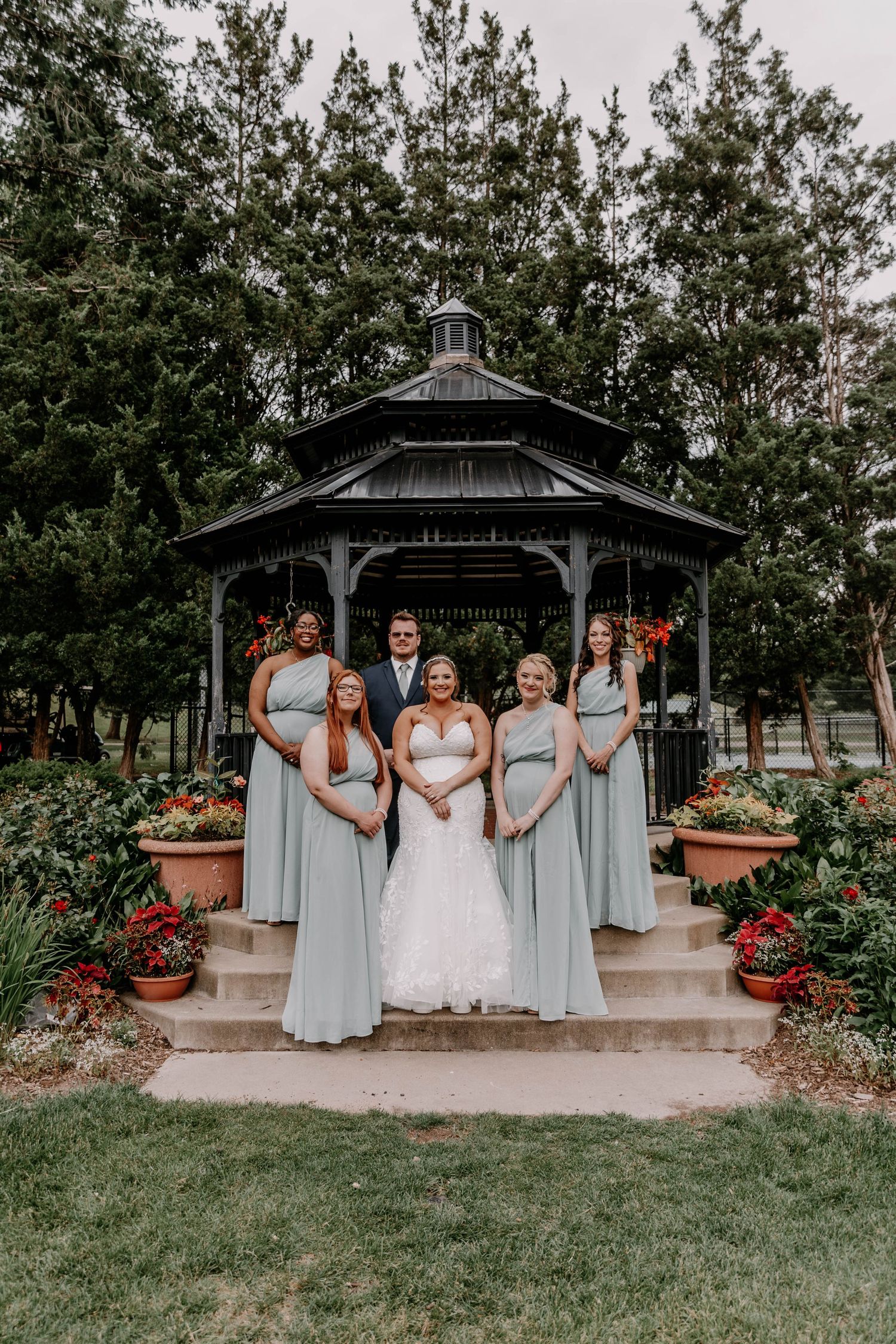 Wedding party poses in a garden gazebo with bridesmaids in light blue dresses and vibrant flowers.