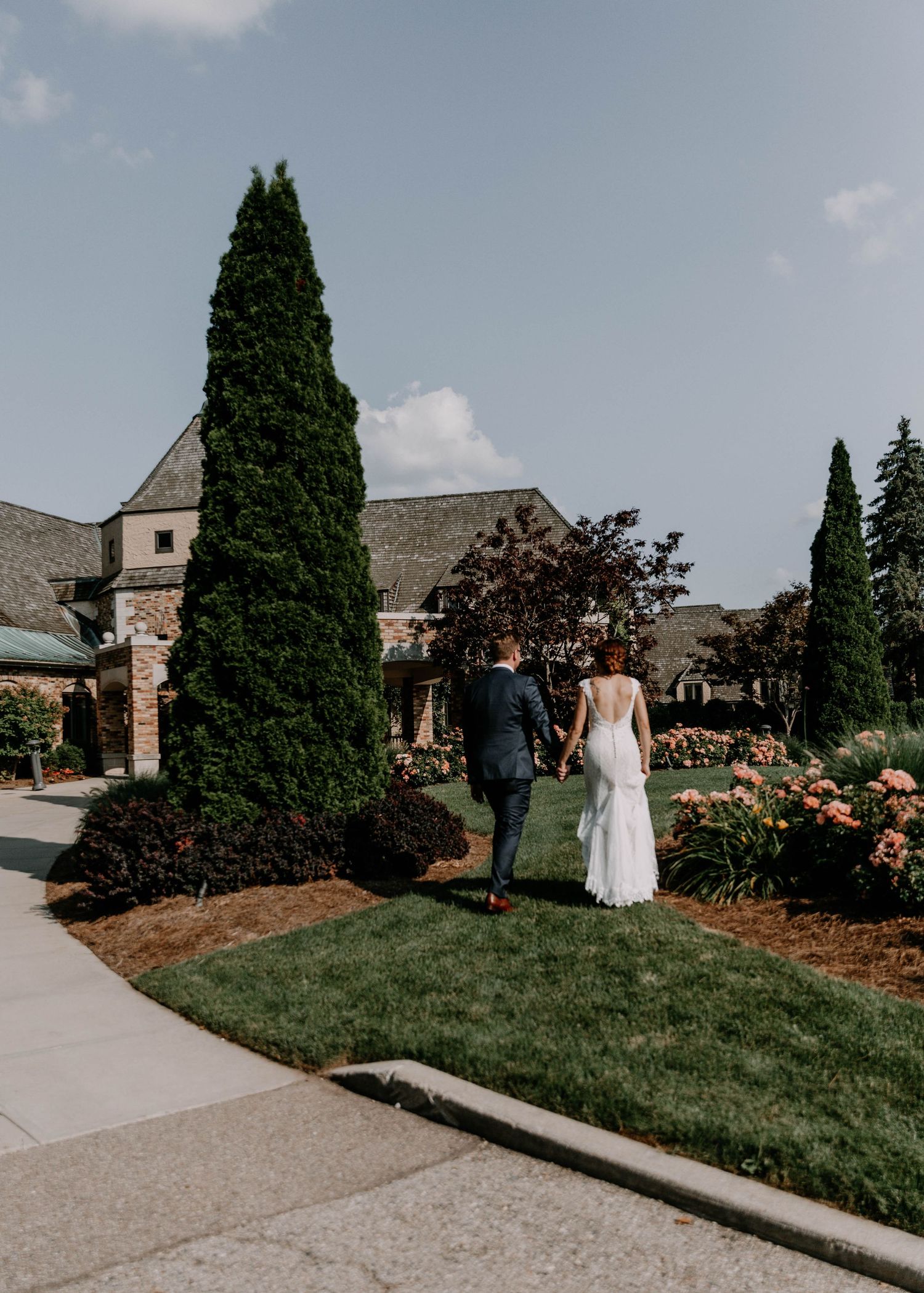 Couple walking through landscaped church gardens with tall cypress trees and stone architecture.