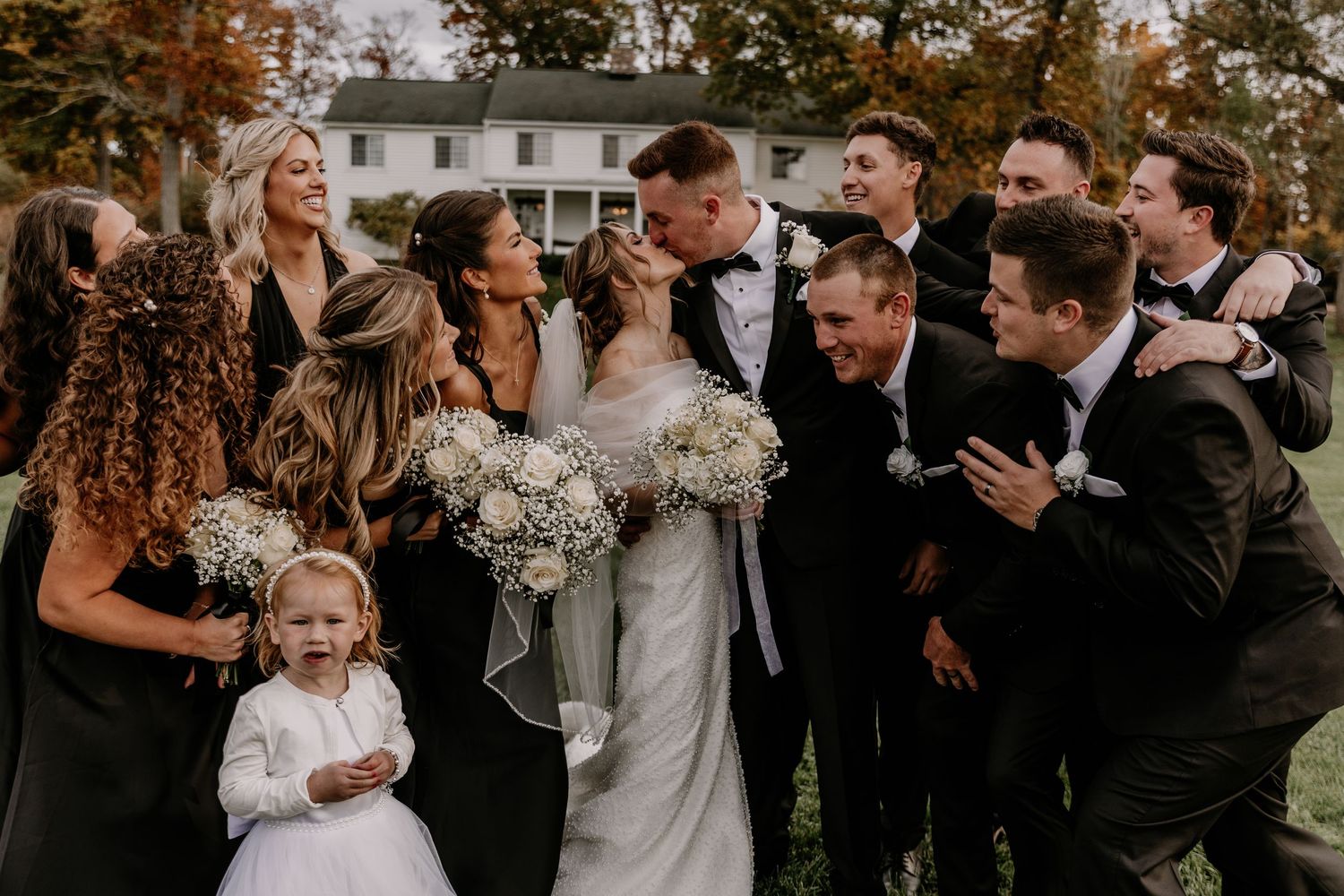 Wedding party laughs and celebrates together outdoors with fall foliage in the background.