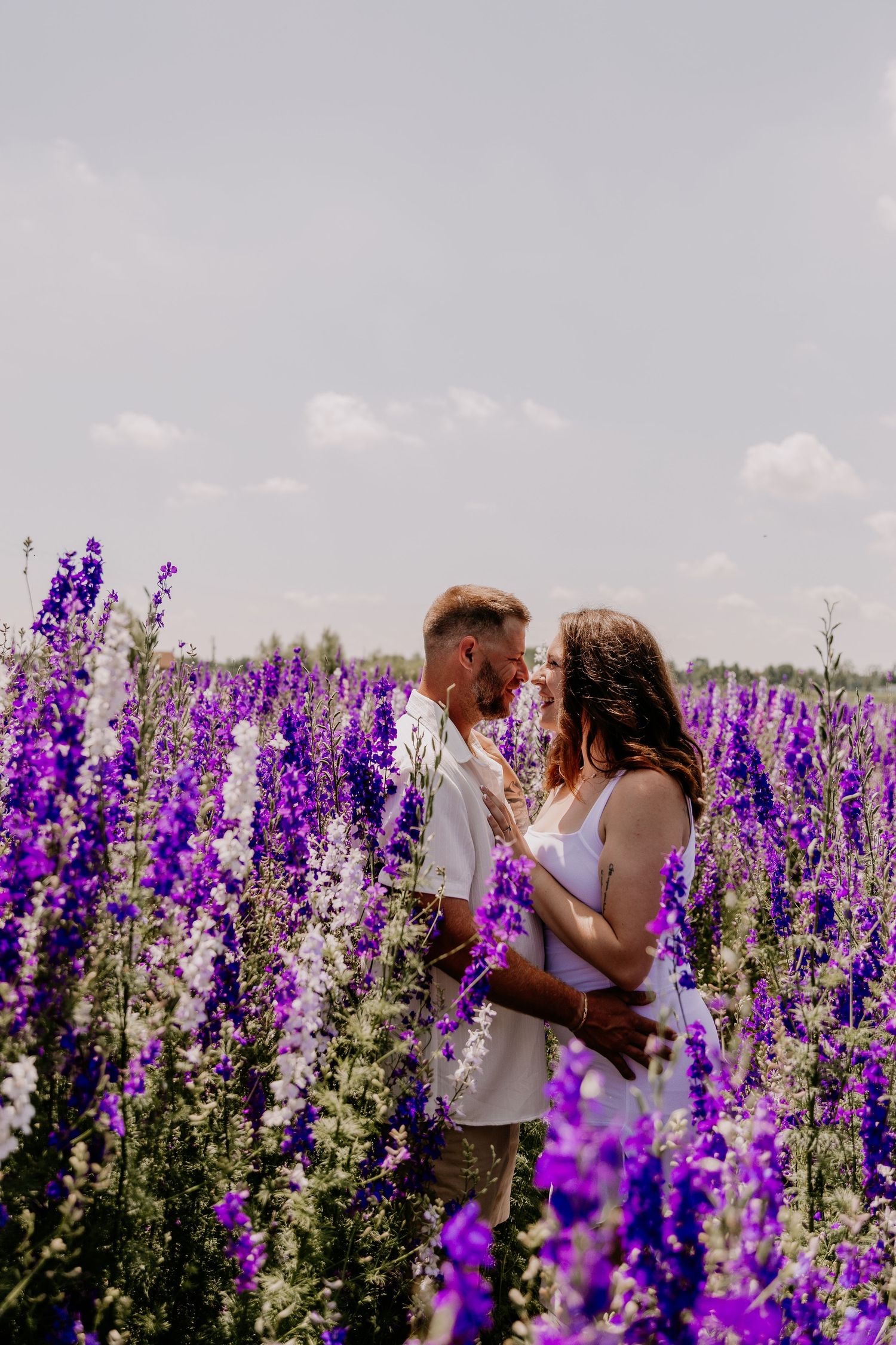 Romantic couple embracing in a vibrant purple lavender field under a cloudy sky on a sunny day.