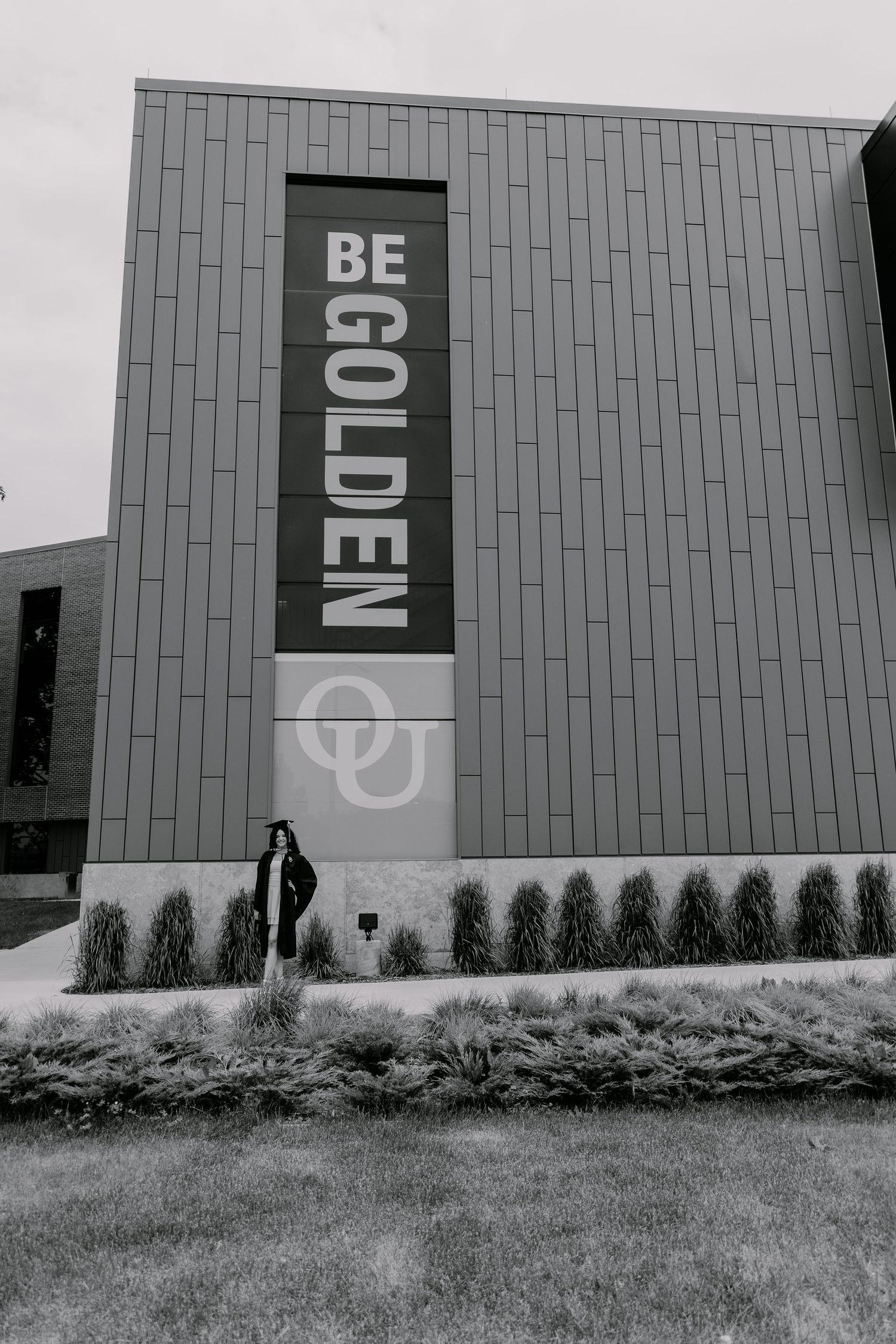 Modern building exterior with vertical 'BE GOLDEN' text signage and gray metal paneling in black and white photography.