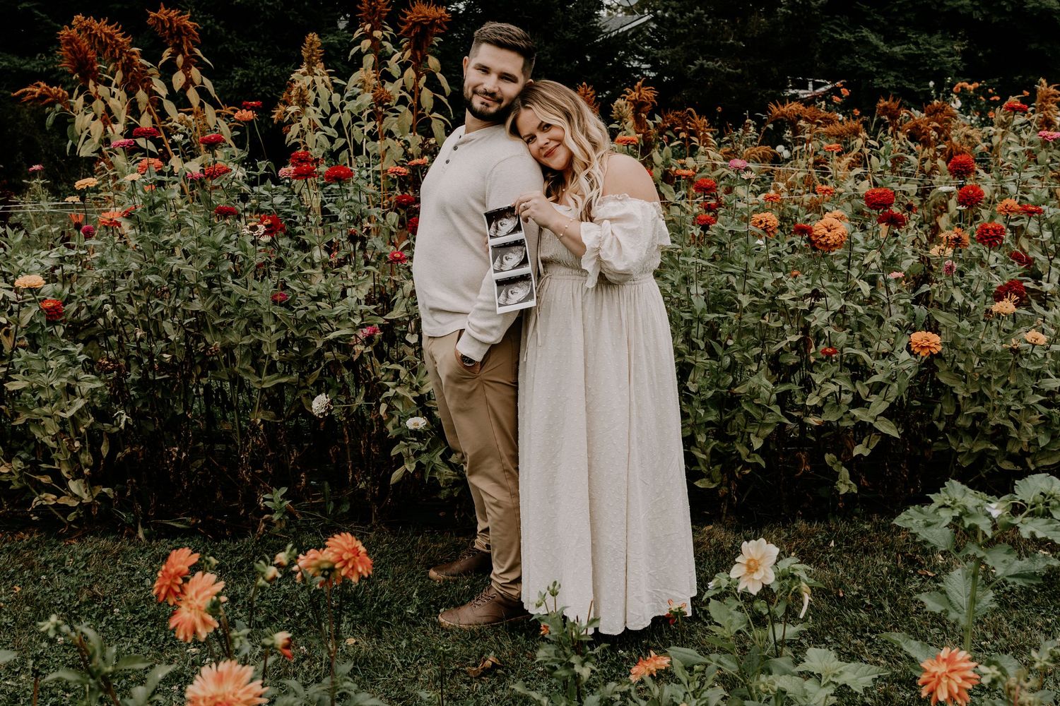 Pregnancy announcement photoshoot in garden with blooming orange and red flowers.