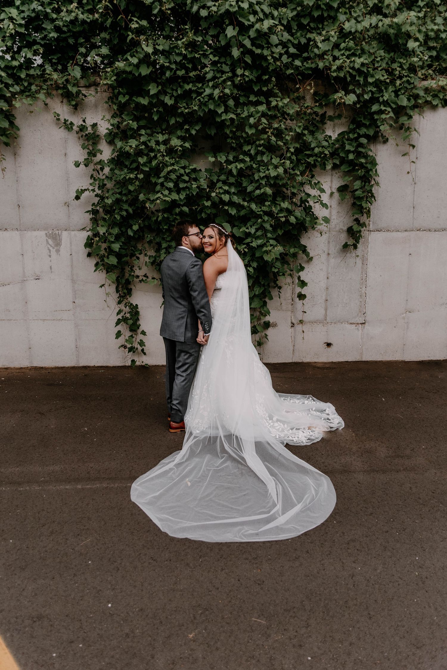 Bride and groom pose for romantic portraits alongside ivy-covered wall outdoors.