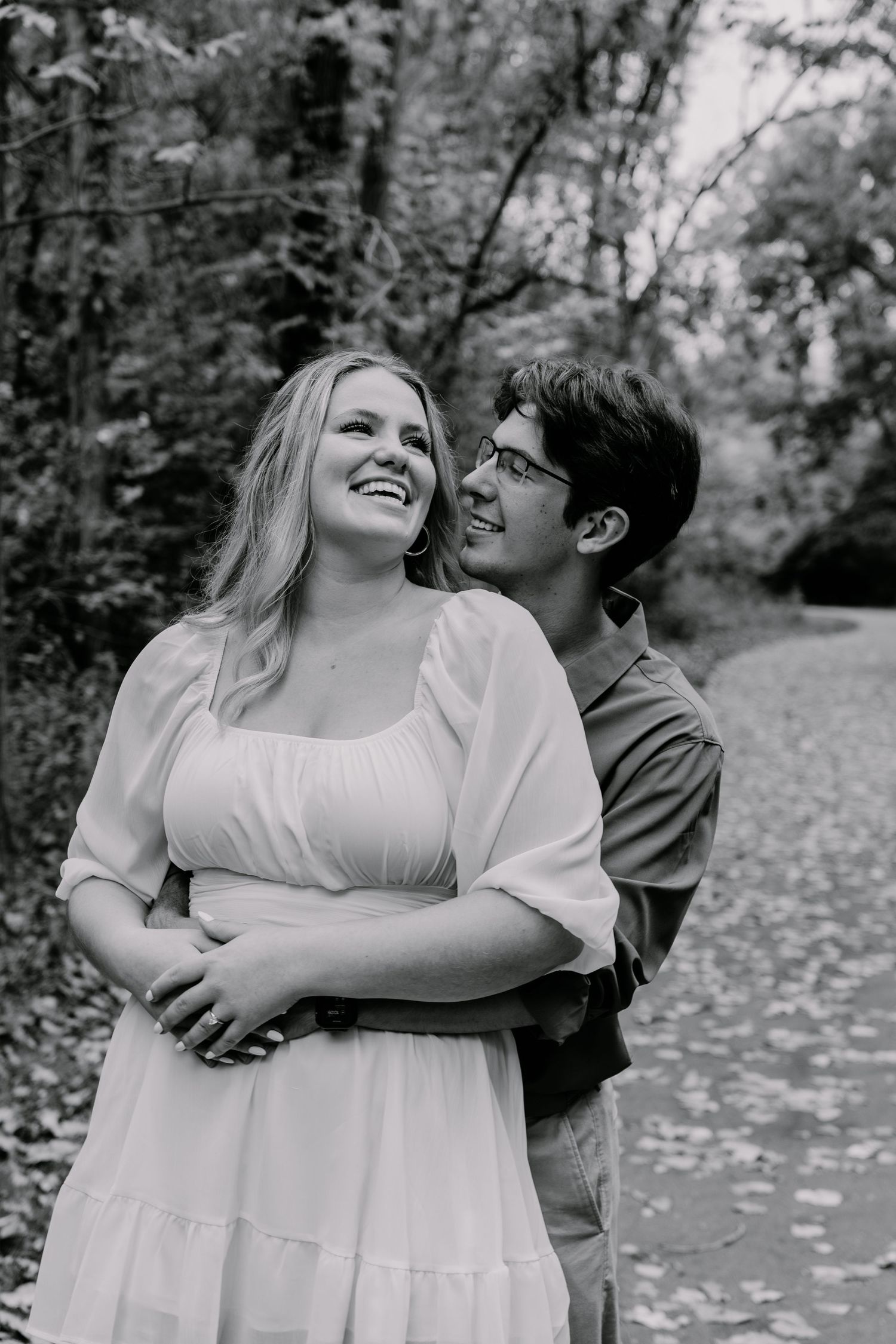 Black and white portrait of happy couple embracing on wooded path.