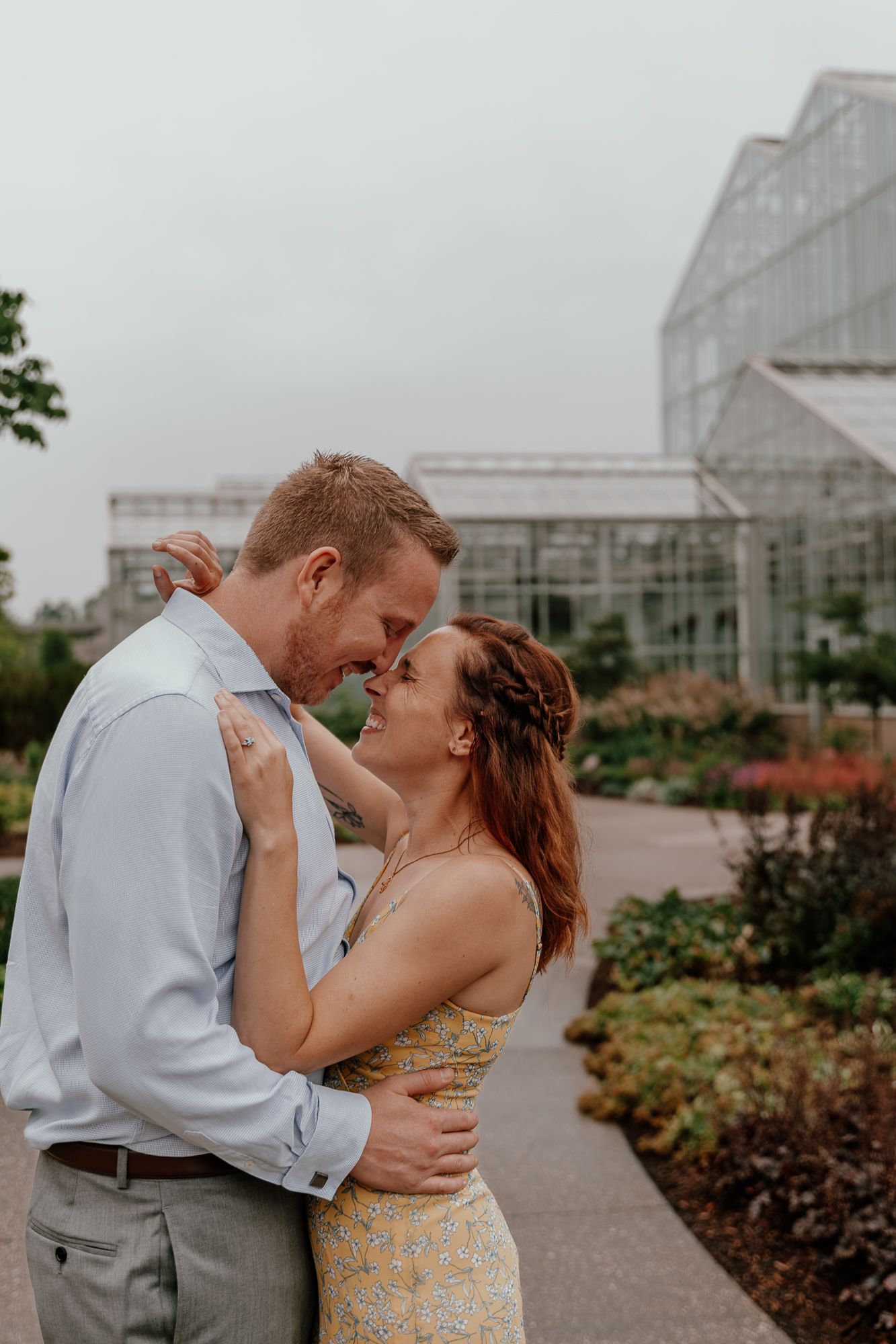 A romantic engagement portrait of a couple in front of a greenhouse with beautiful gardens.
