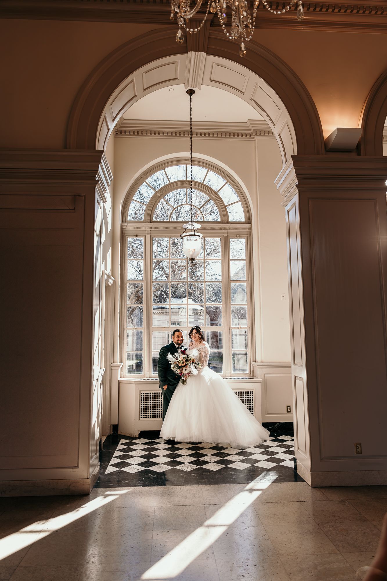 A wedding couple framed by an arched doorway with checkered floors and elegant architectural details.