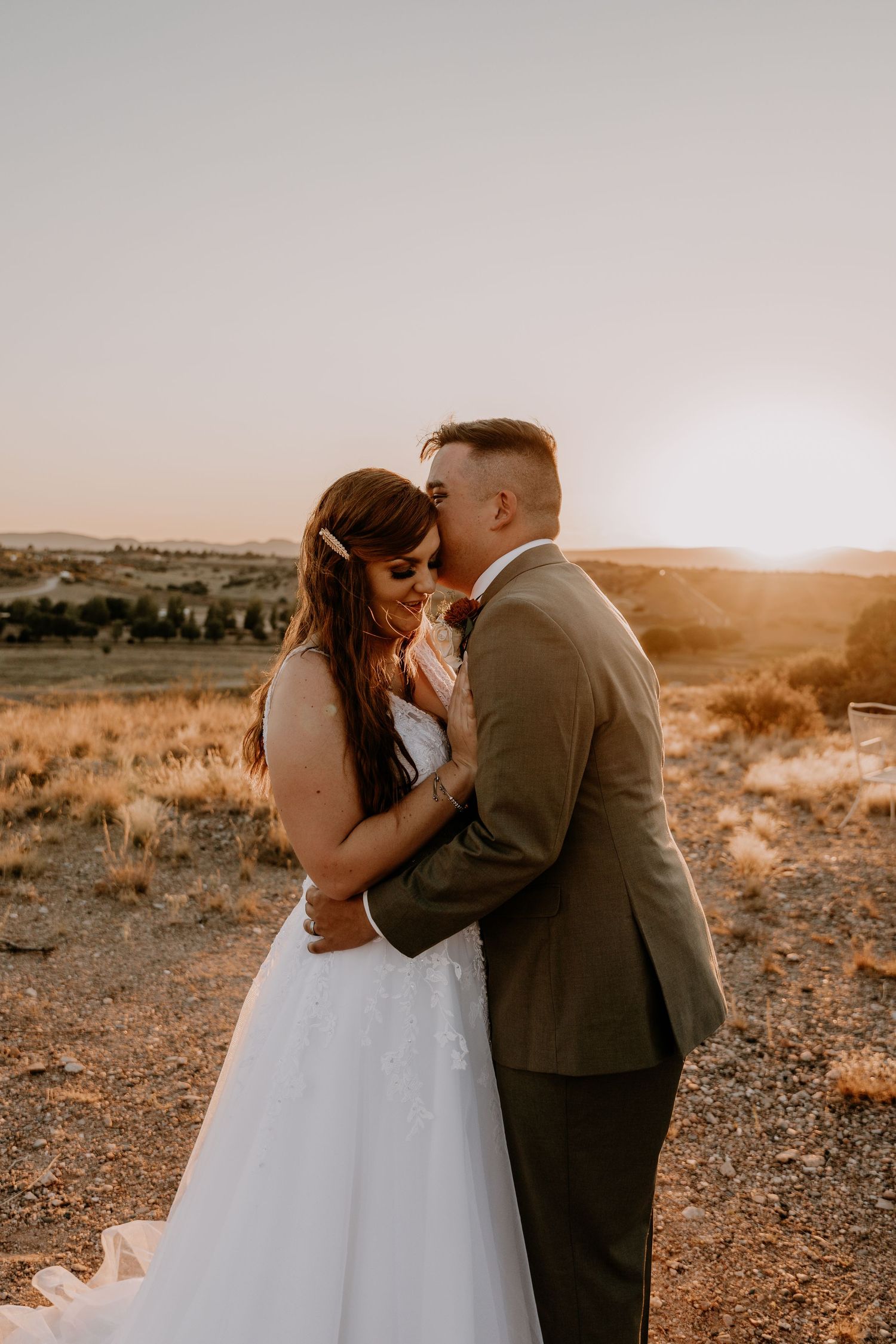 Bride and groom share a romantic moment at sunset in a desert landscape.