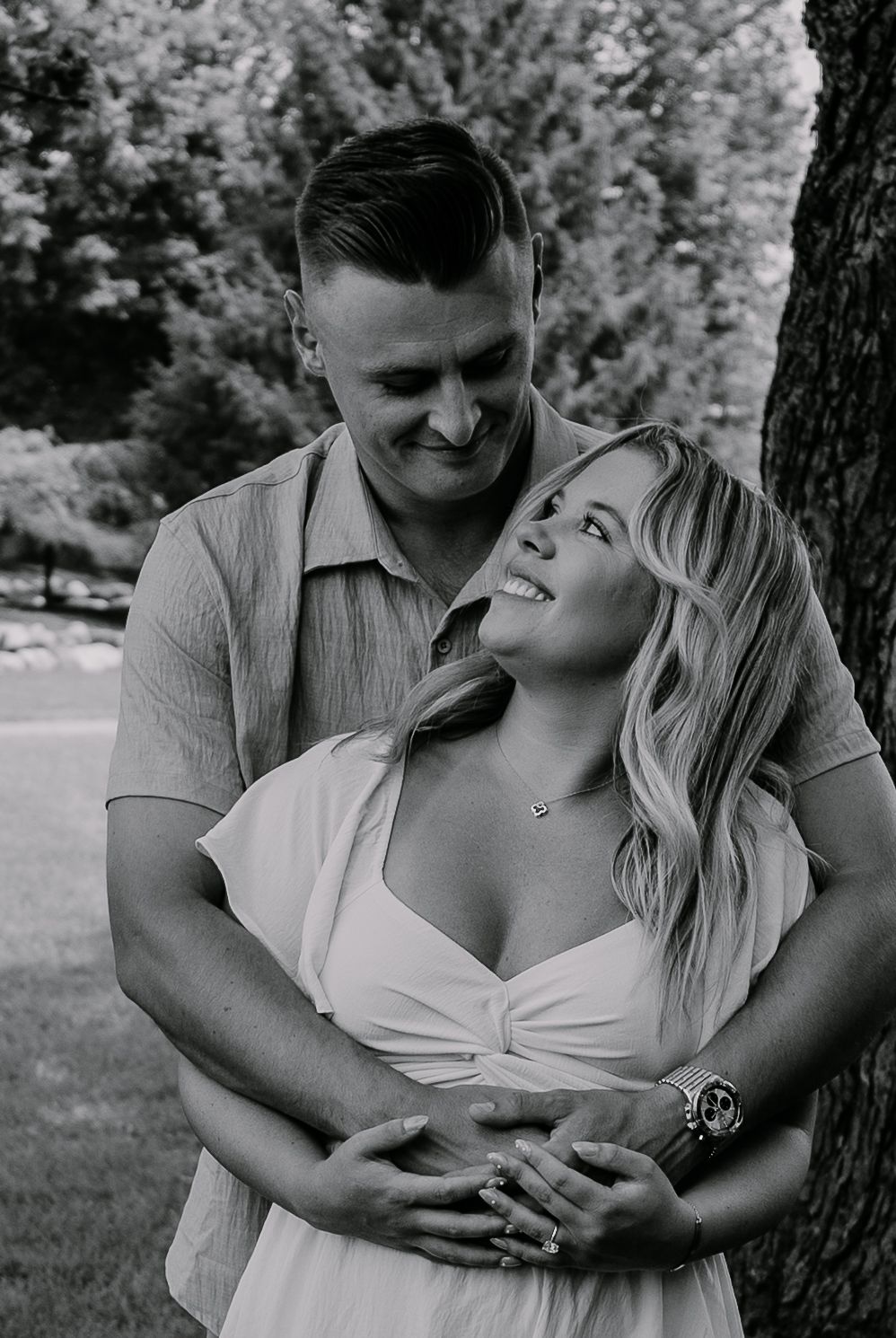 Black and white romantic portrait of a couple embracing outdoors while sharing a joyful candid moment in a garden setting.