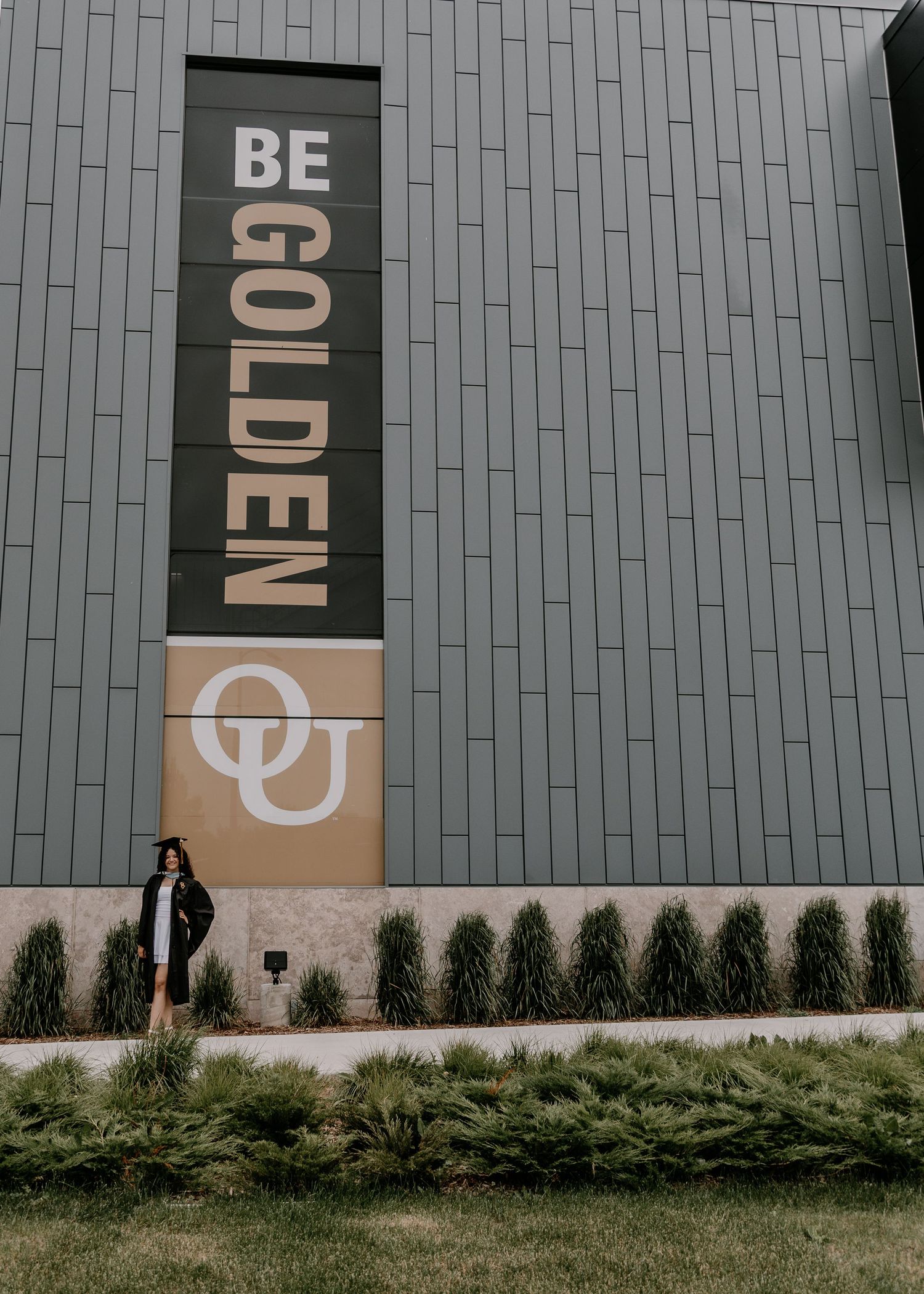 A modern building exterior features vertical metal panels with 'BE GOLDEN' signage and decorative landscaping.