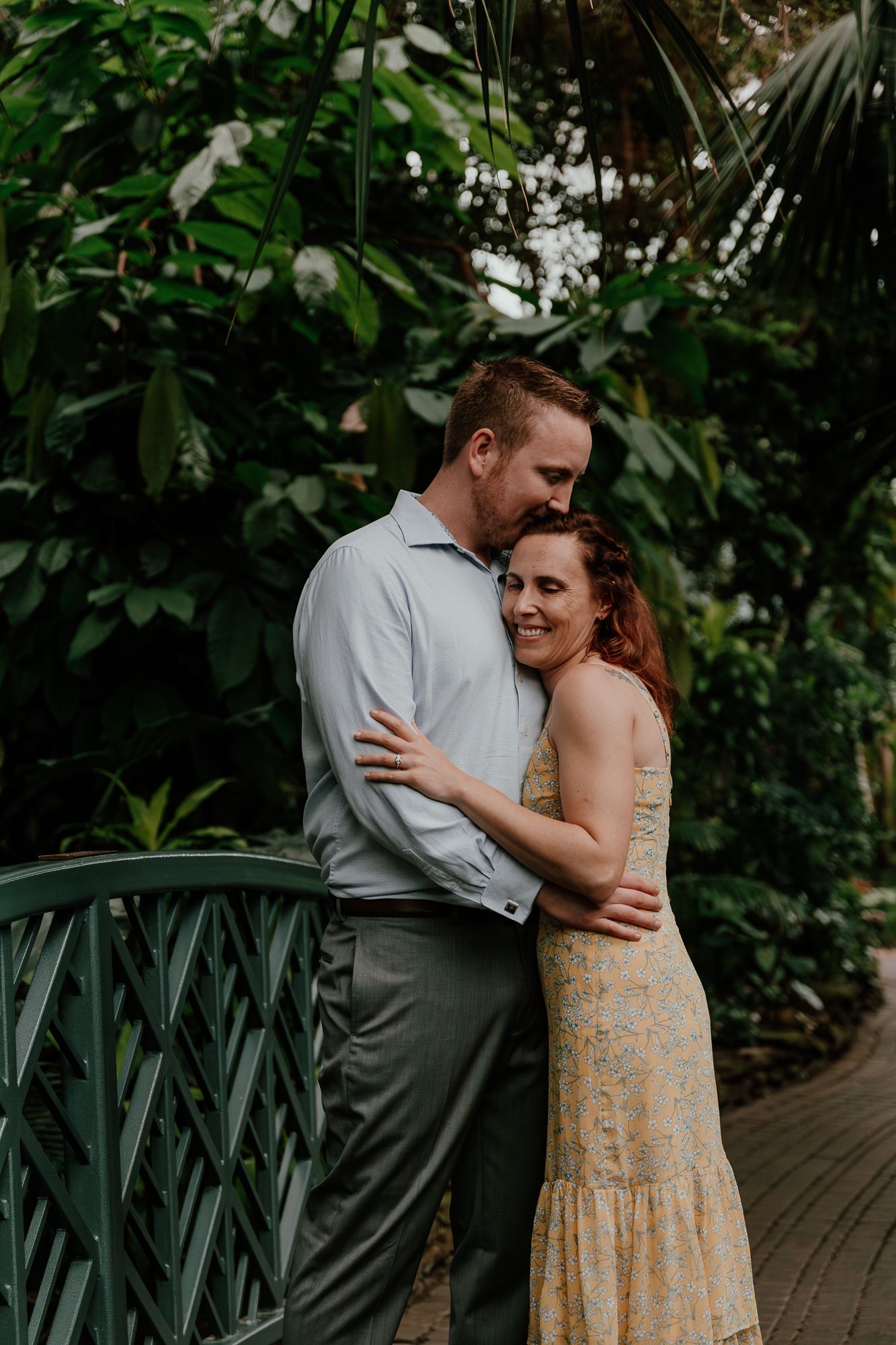A couple sharing an intimate moment on a bridge surrounded by lush greenery.