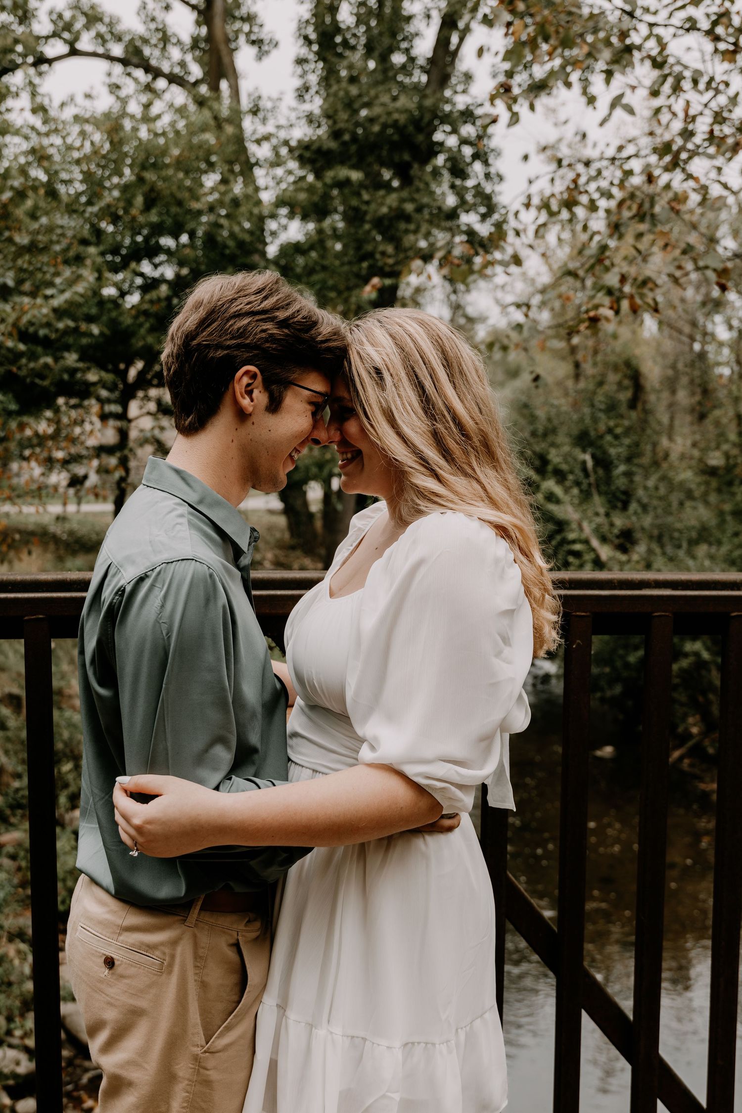 A couple shares an intimate moment on a wooden deck surrounded by autumn trees.