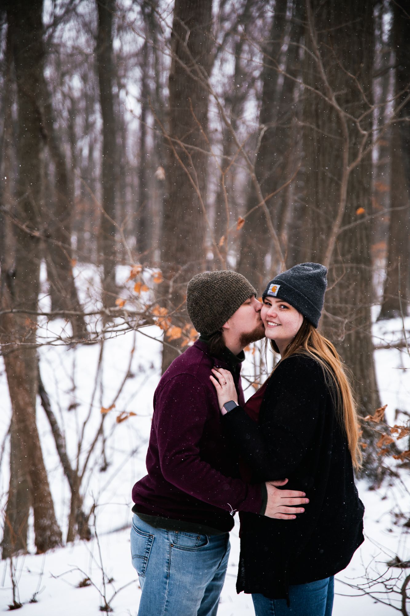 Romantic photoshoot in a snow-covered forest with couple holding a white blanket.