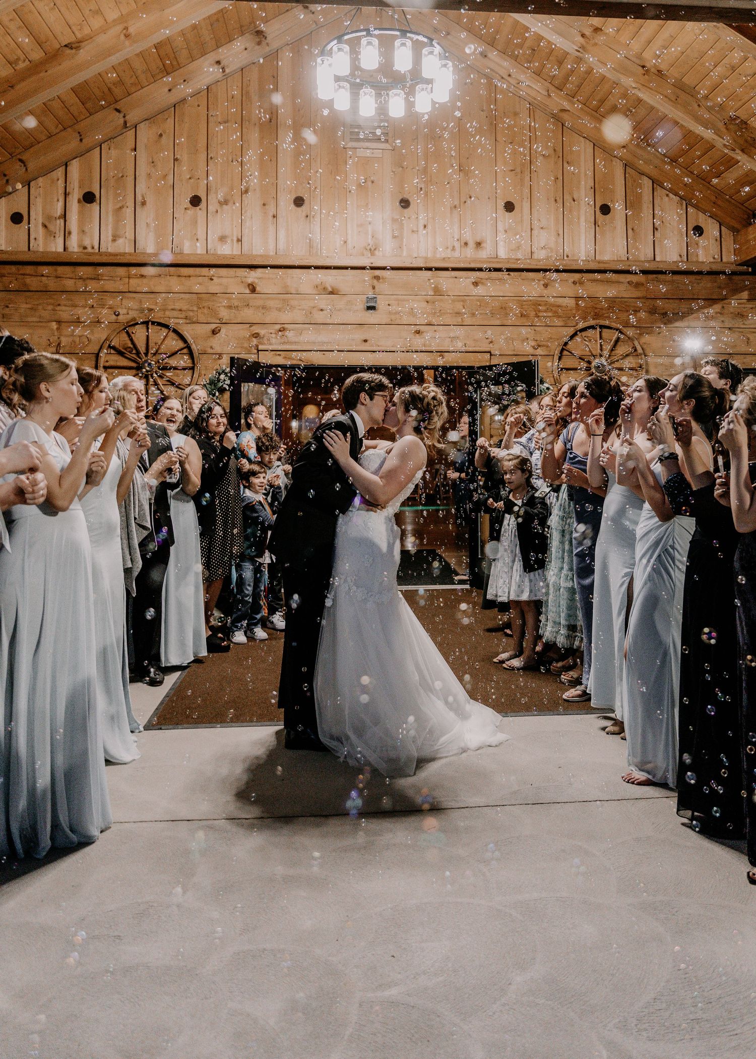 Wedding party and guests form aisle for newlyweds during celebratory moment in rustic barn venue.