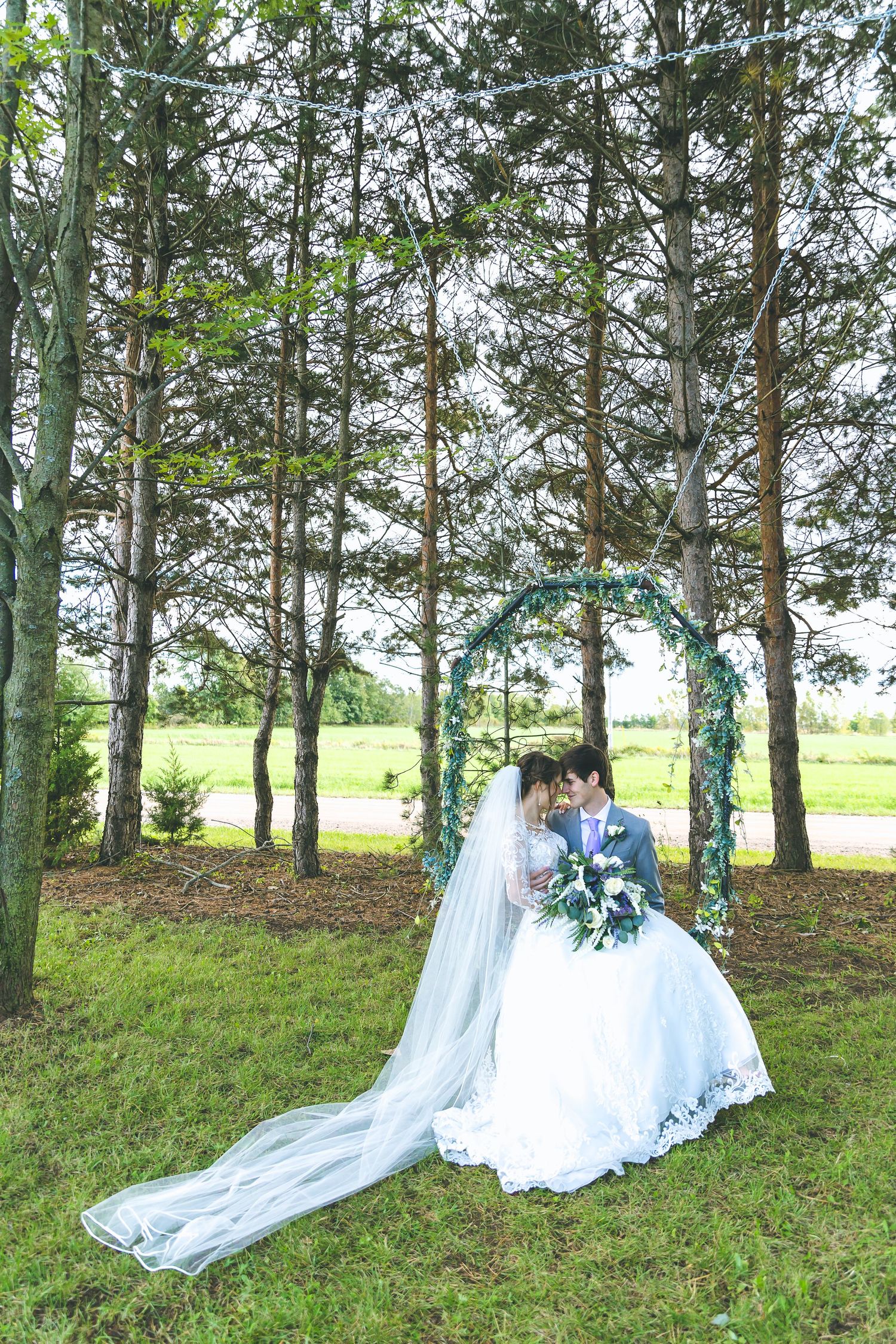 Wedding couple poses among tall birch trees with flowing veil trailing behind.