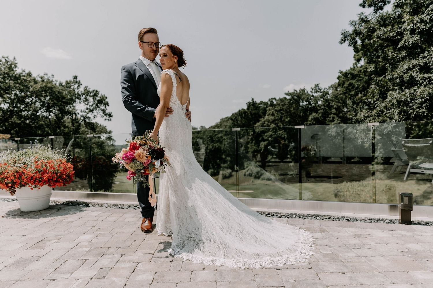 Bride and groom share tender moment on outdoor terrace with flowing wedding dress train.