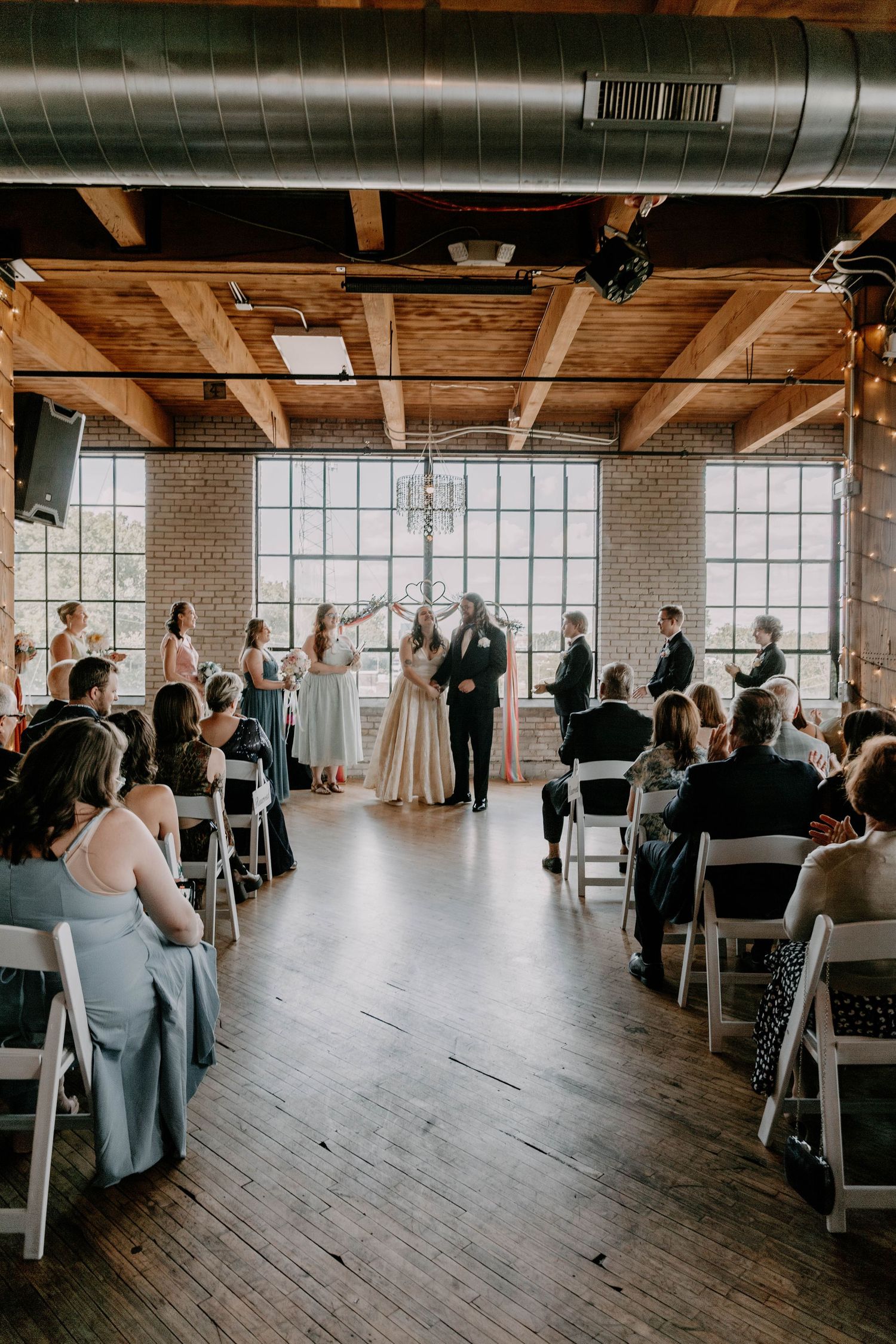 Wedding ceremony in progress in industrial venue with exposed brick and wooden beams.