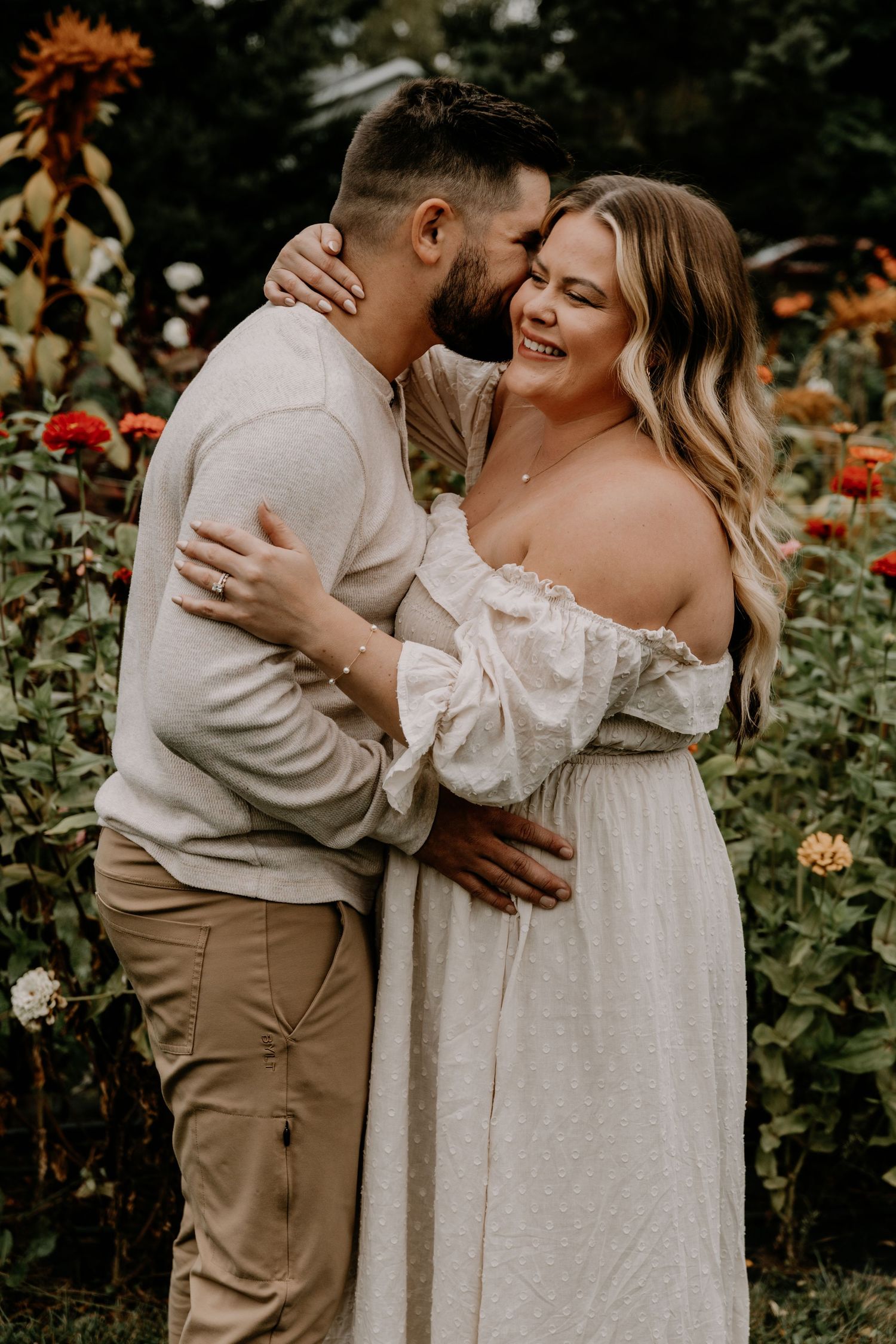 Tender embrace captured in a garden setting with white dress and neutral tones.