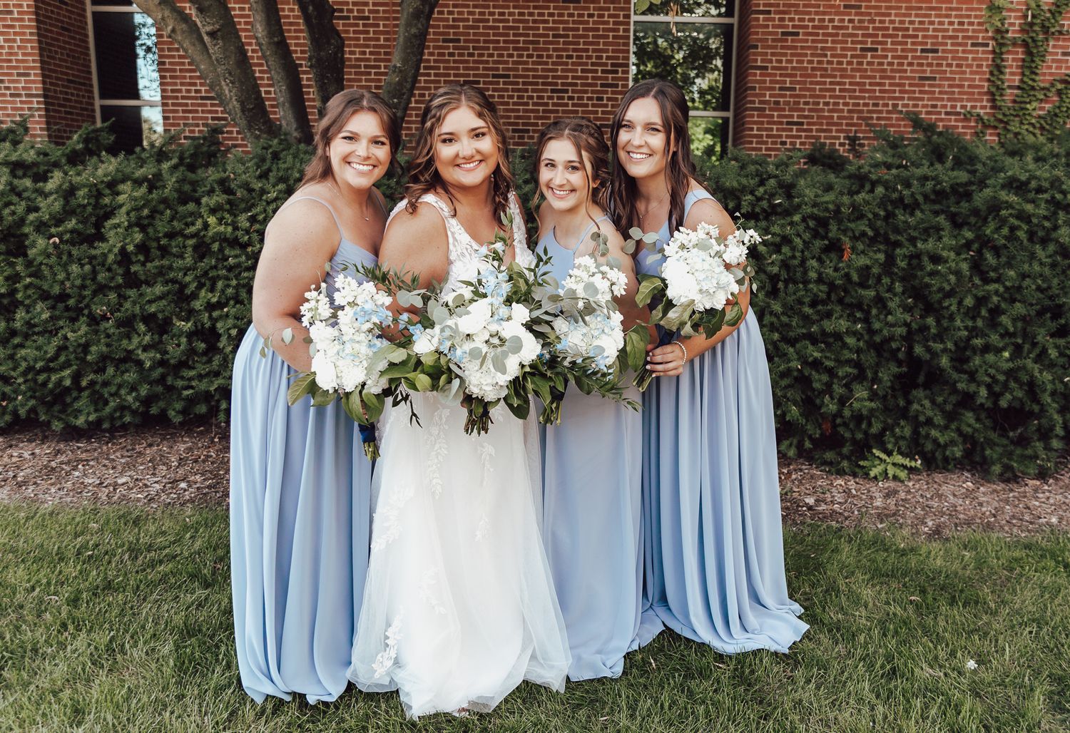 Bride poses with bridesmaids in light blue dresses holding white floral bouquets.