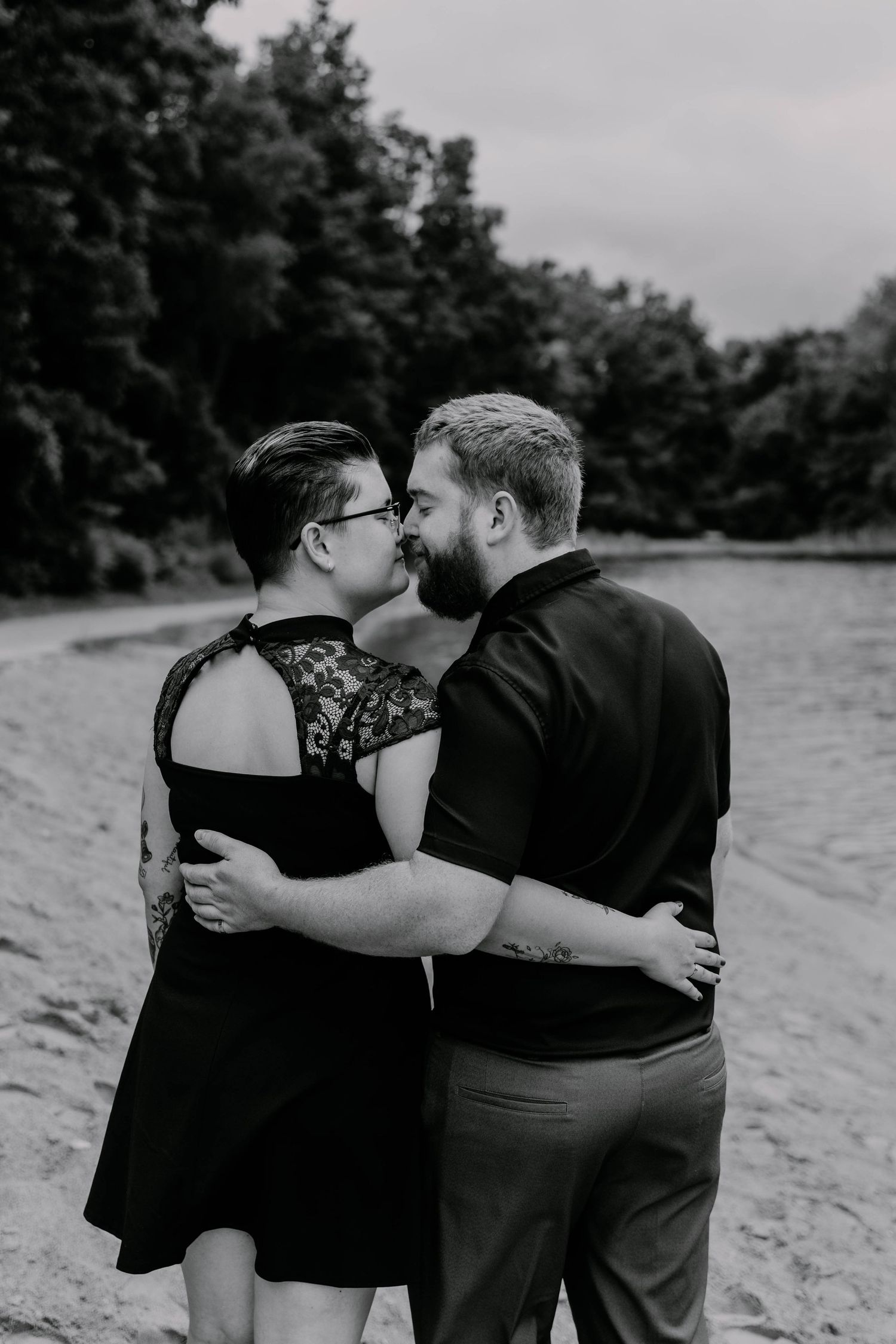 Intimate black and white portrait of couple embracing on beach with waterfront view.