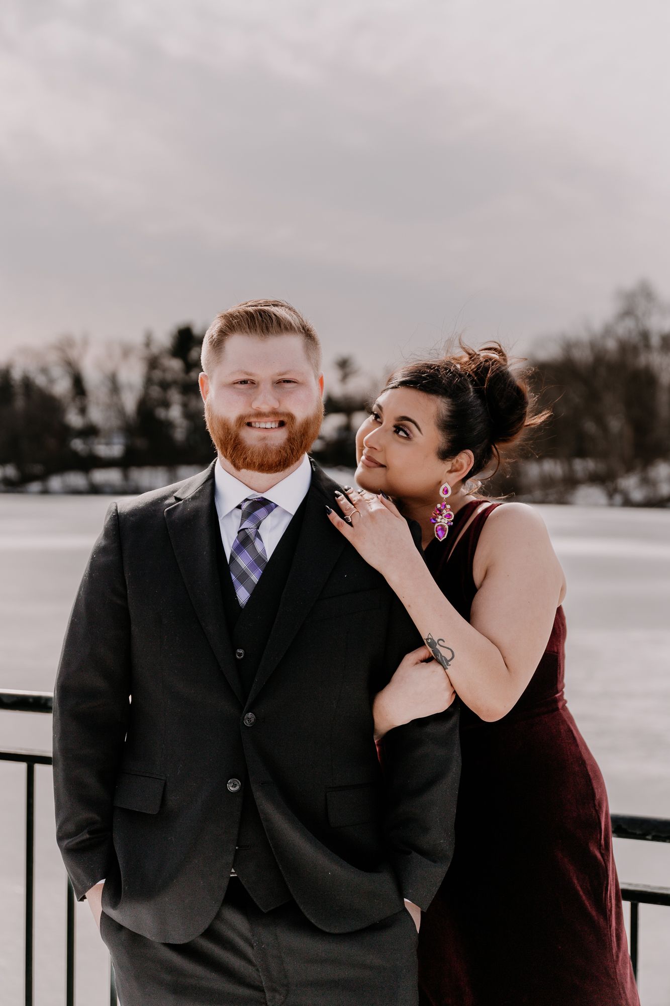 A couple in winter formal wear posing playfully against a snowy backdrop.