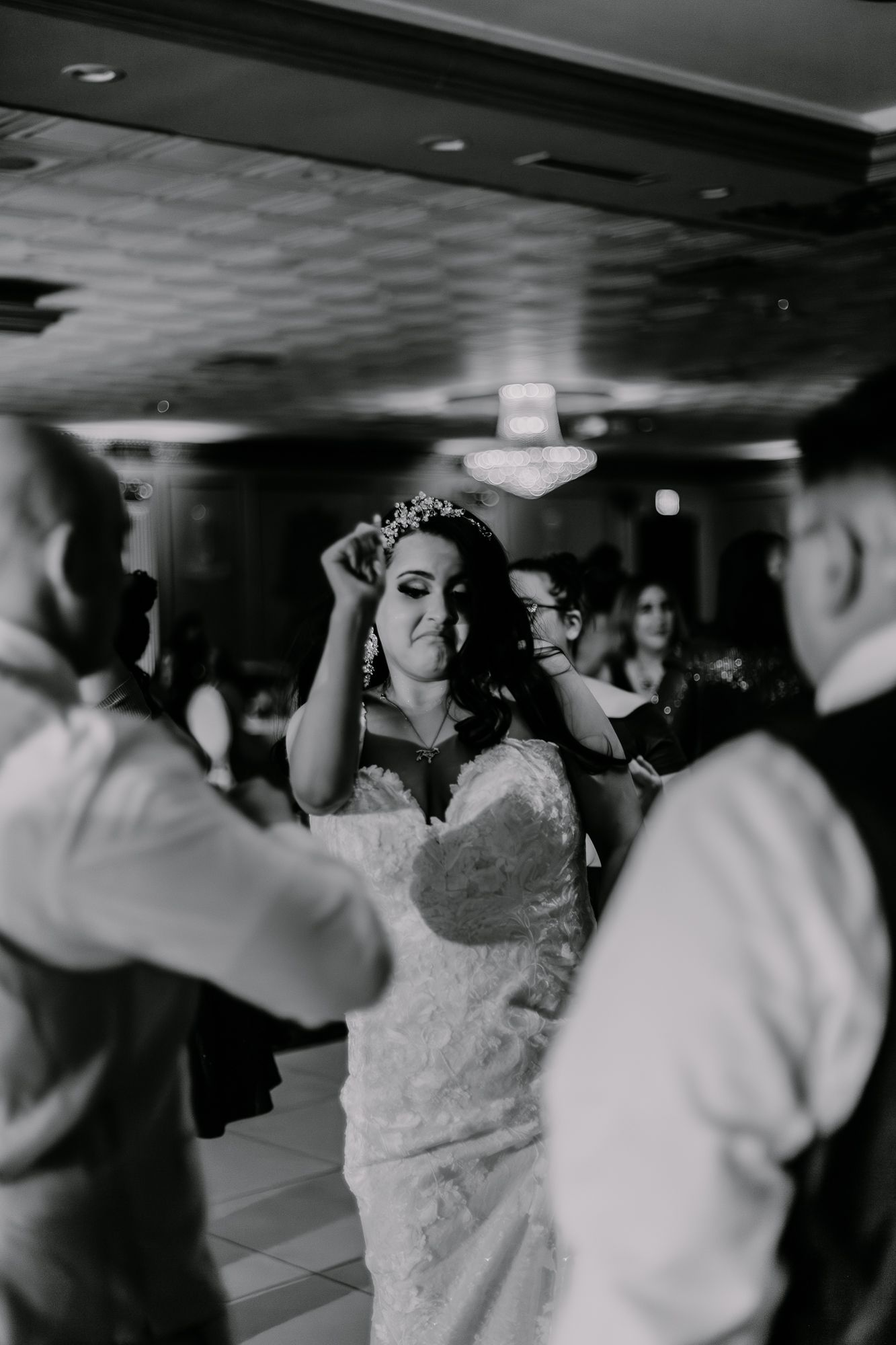 A bride in a white lace gown dances at her wedding reception with a crown on her head.