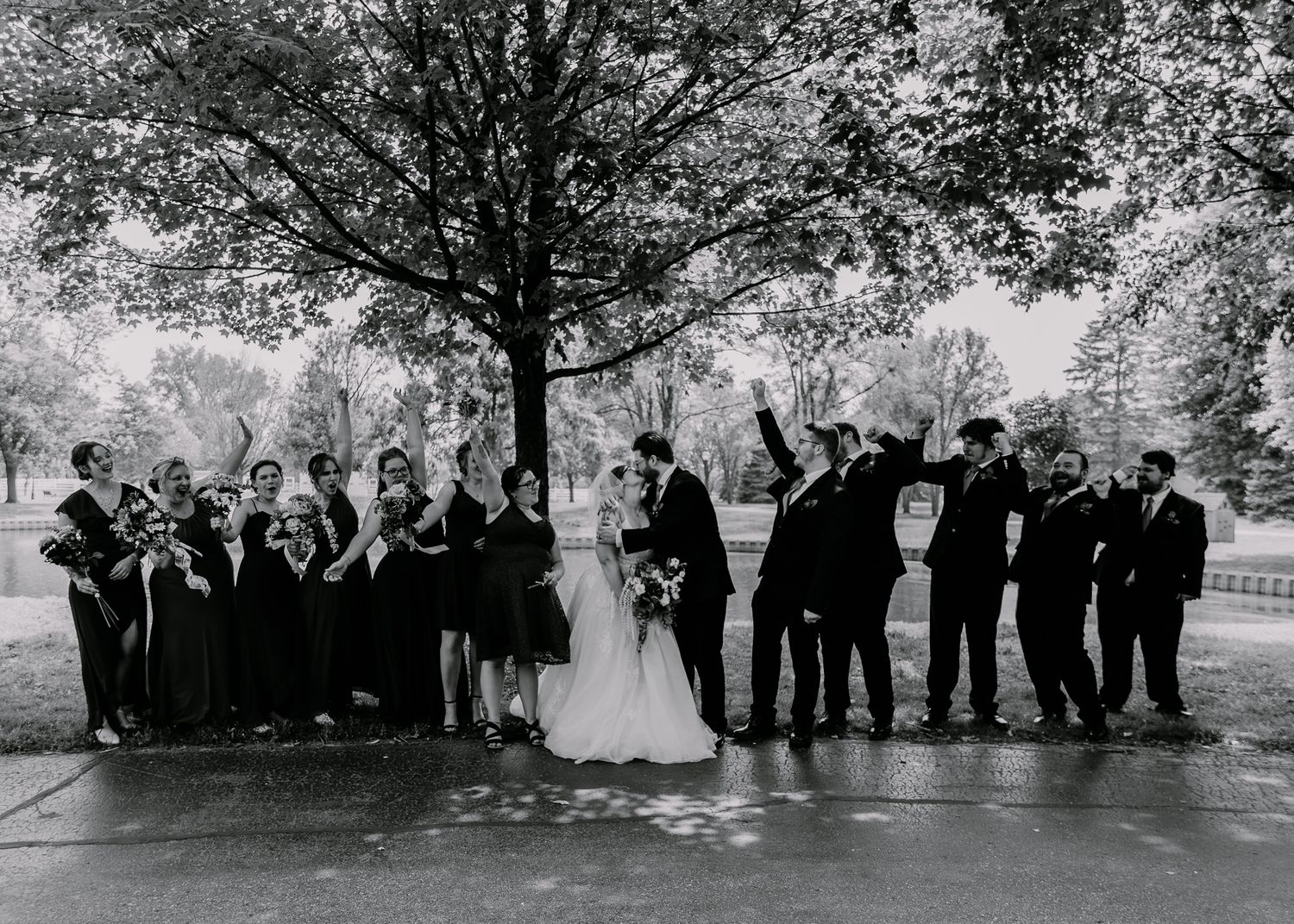 Wedding party poses under tree canopy in black and white photography.
