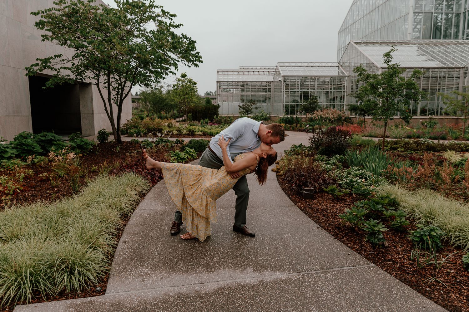A romantic dip pose during an engagement photoshoot in front of a modern glass building.
