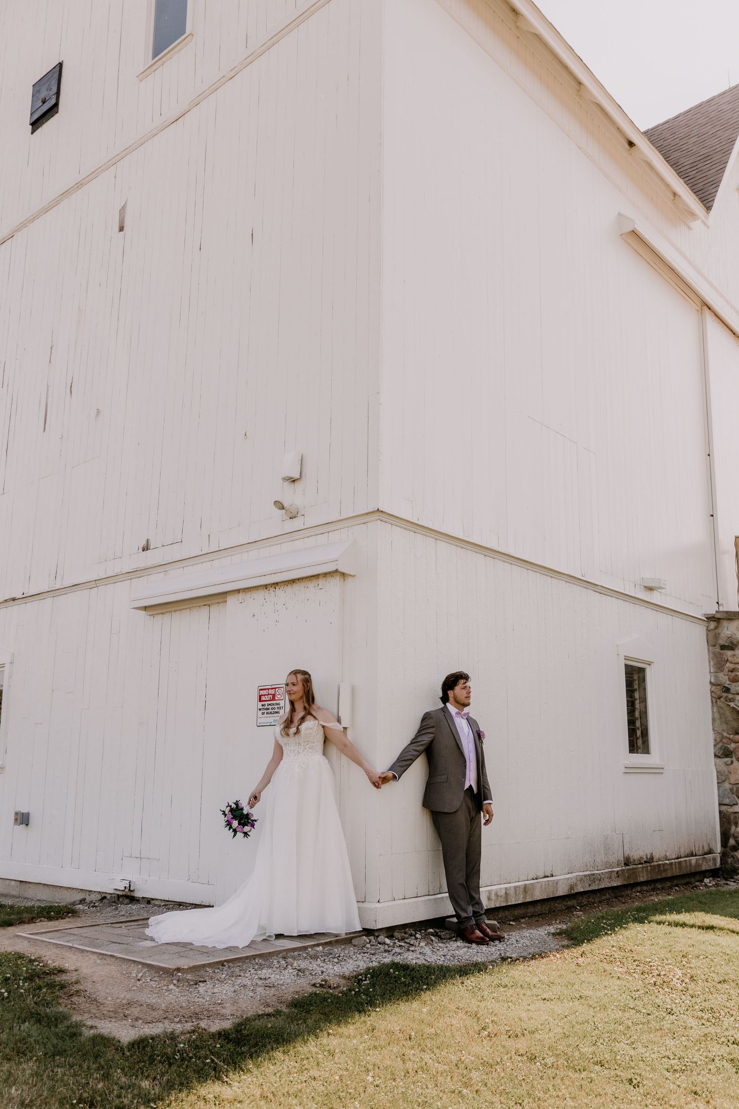 Bride and groom hold hands outside a white barn venue on their wedding day.
