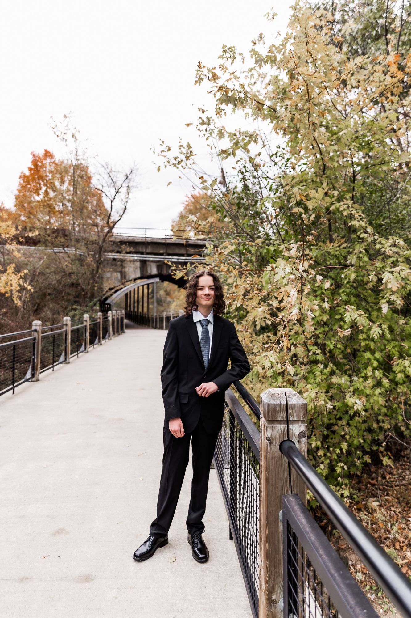 Person in black suit standing on bridge walkway during autumn season.