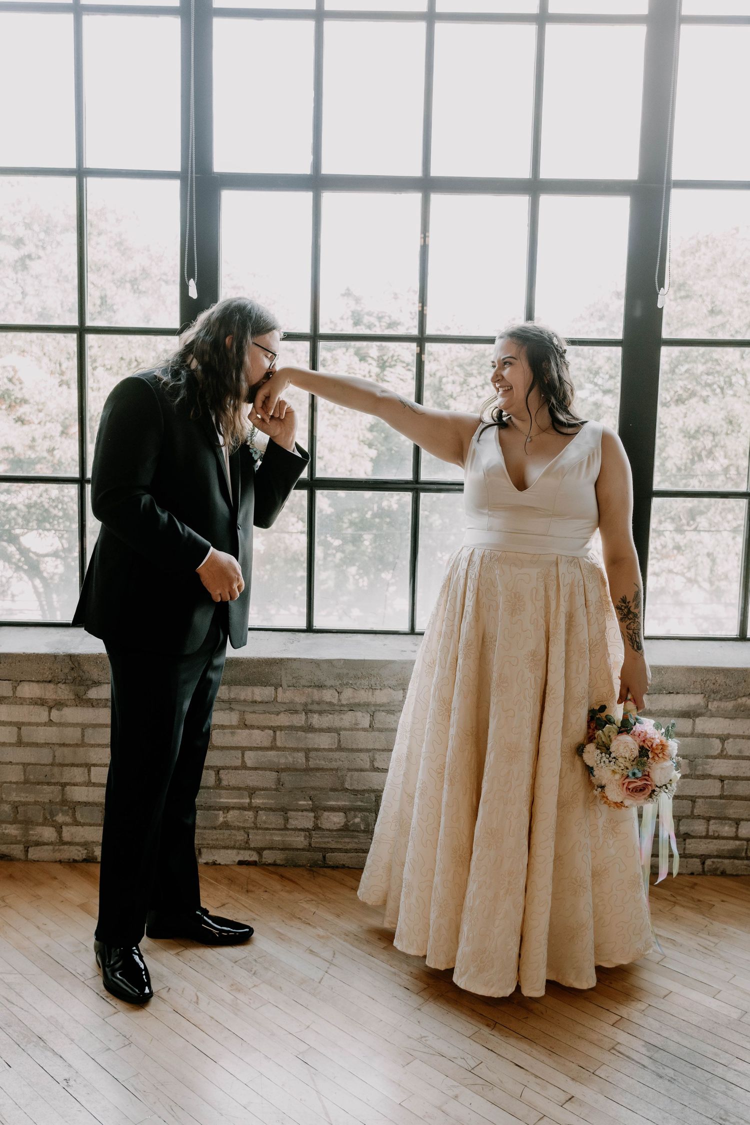 A playful moment between newlyweds in front of large windows in an industrial venue.