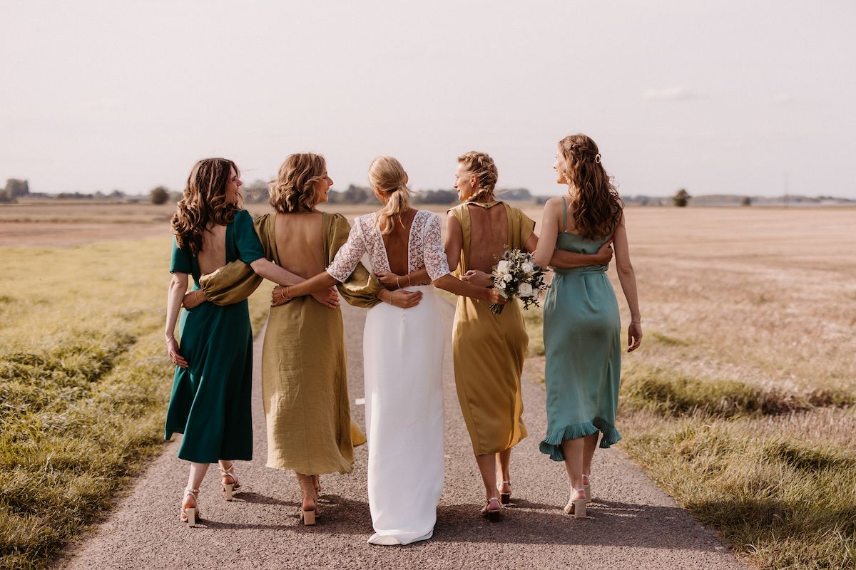 Wedding party walking together through a golden field at sunset wearing earth-toned dresses.