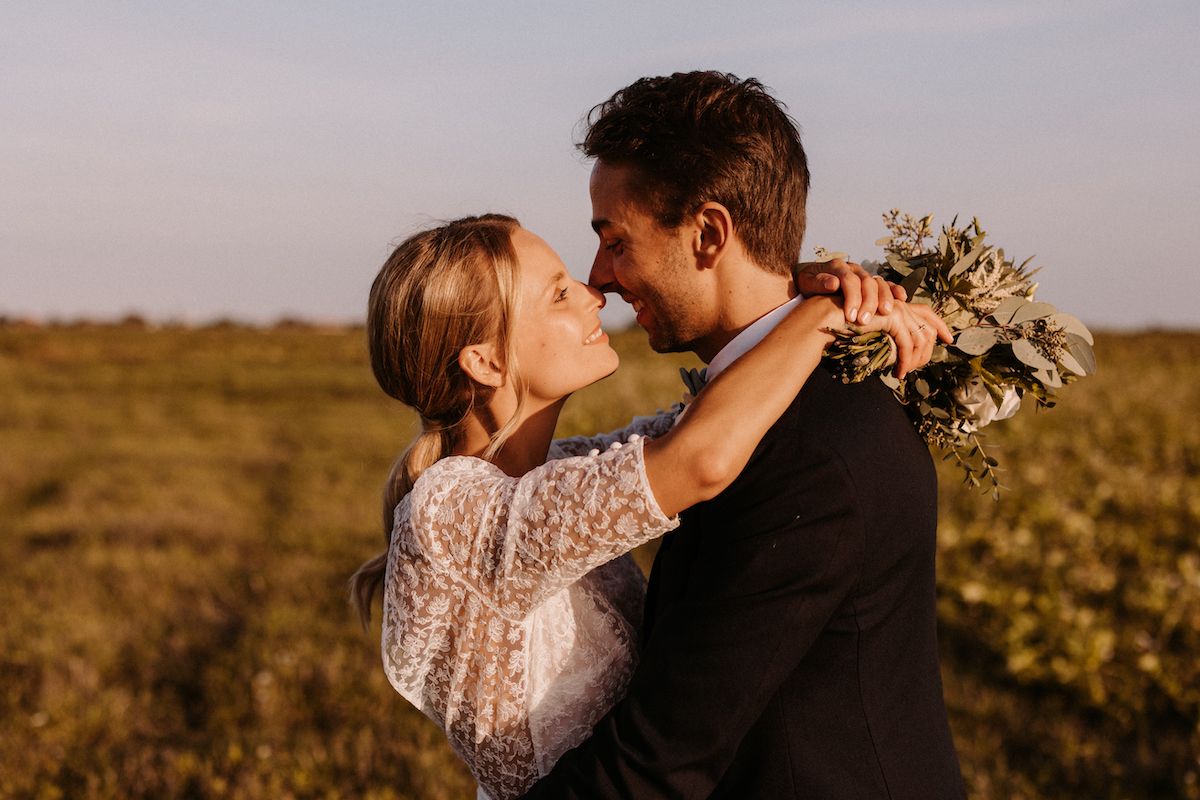 A romantic sunset embrace between newlyweds in a field with lace dress details.