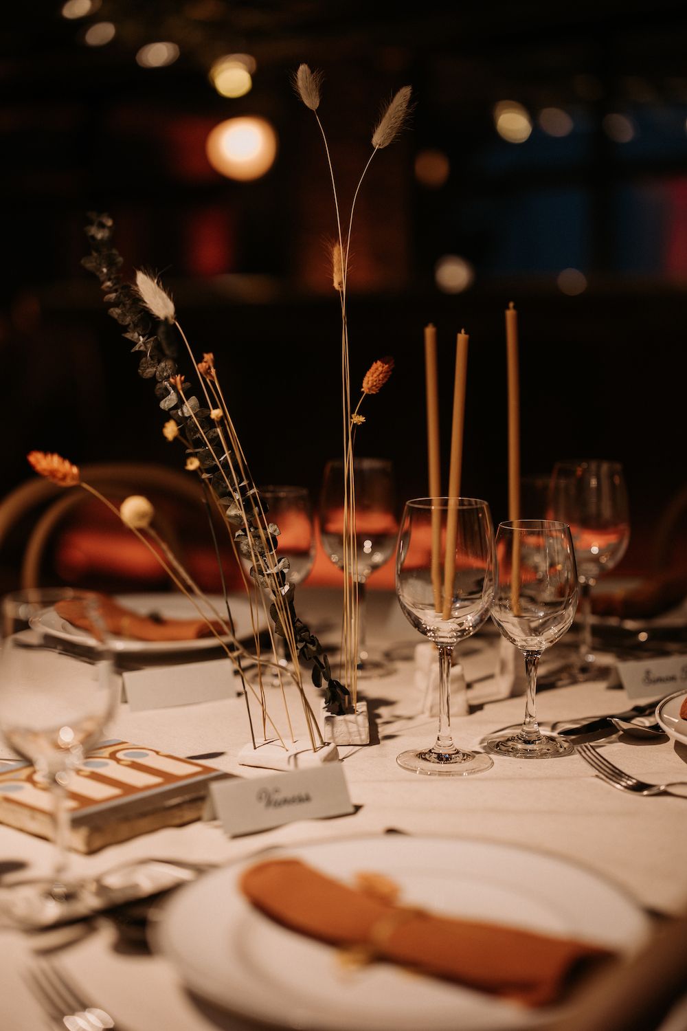 Intimate table setting with wheat stalks and wine glasses in warm ambient lighting.