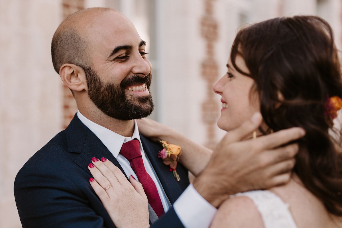 An intimate wedding photo showing newlyweds laughing together against a light background.