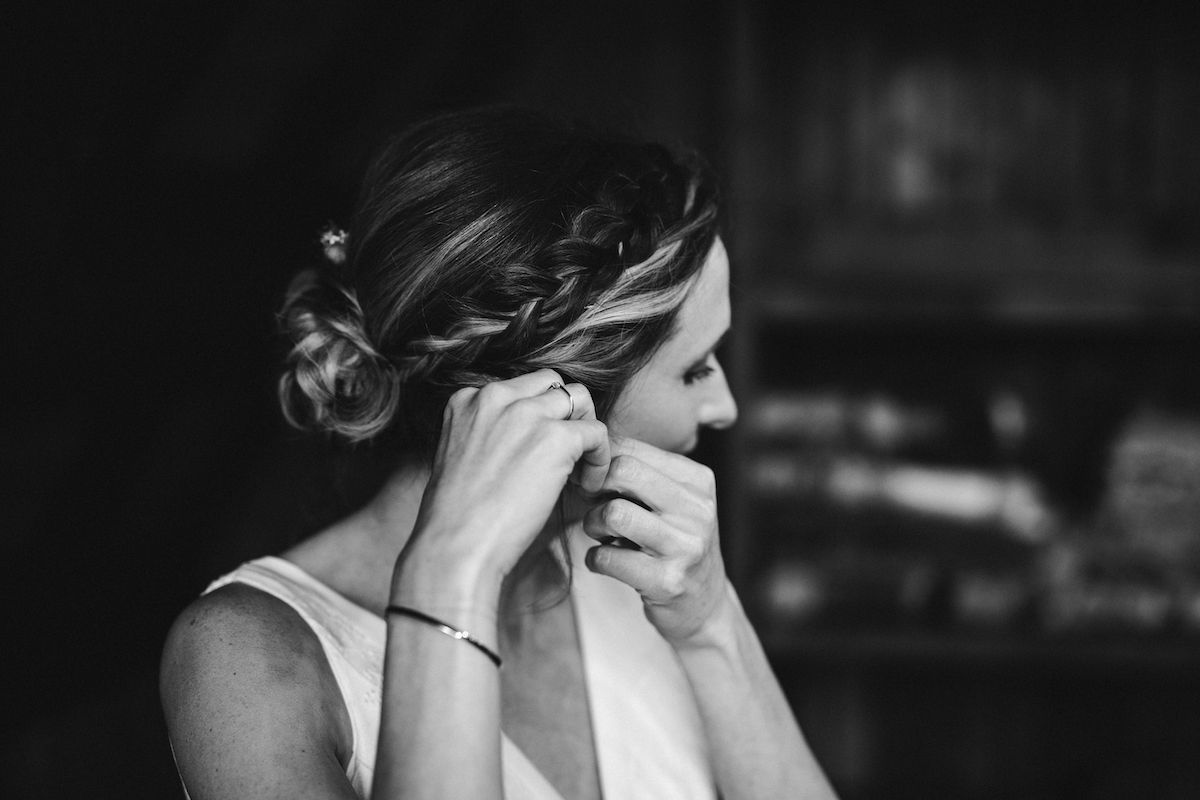A black and white photo of a bride putting on earrings during wedding preparations.