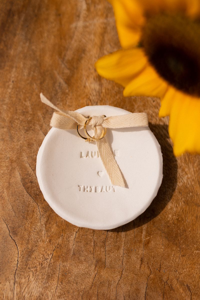 White ceramic wedding ring holder with ribbon detail on rustic wooden table.