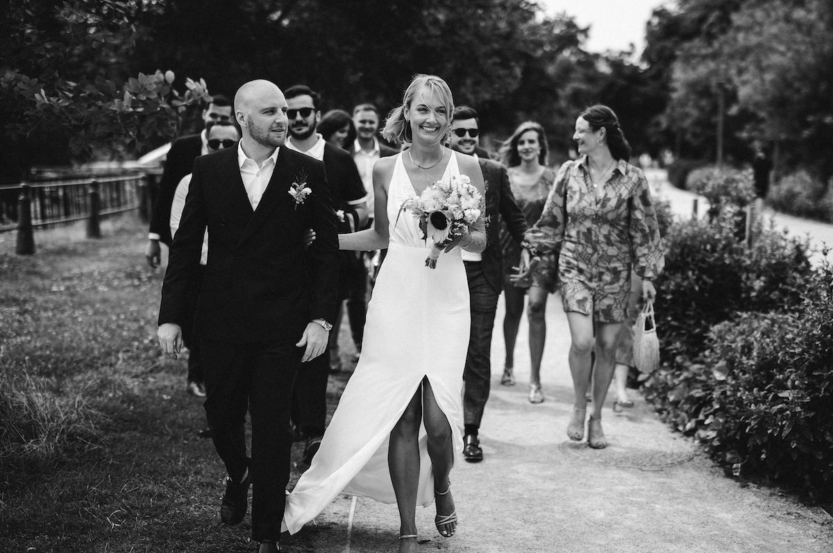 Wedding party walks along garden path during outdoor celebration.