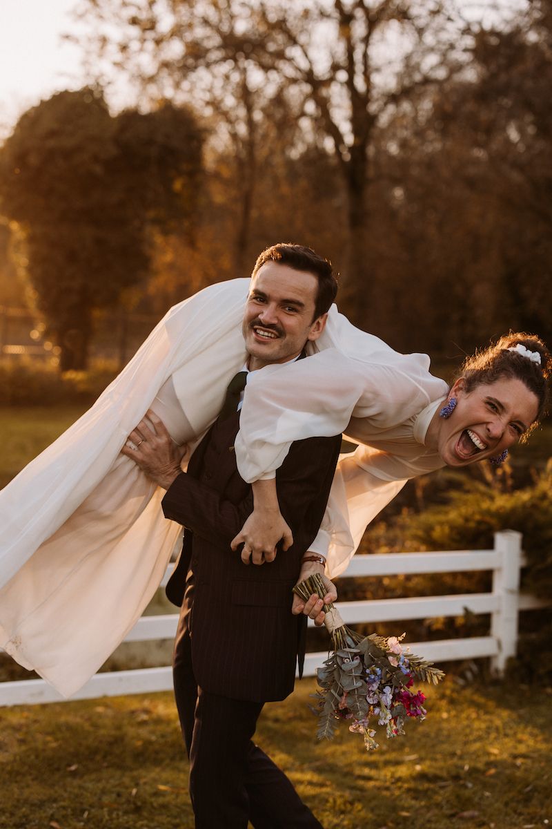 Playful wedding moment in golden sunlight with couple near white fence.