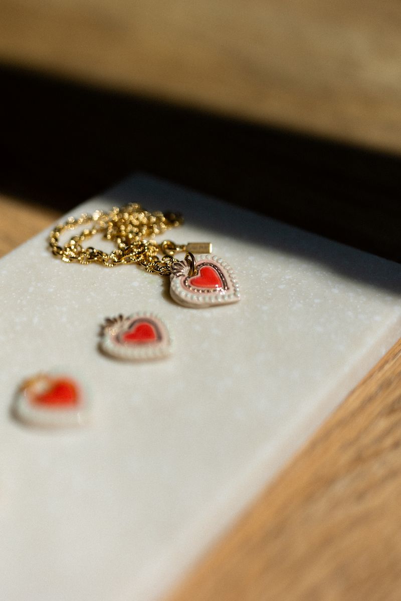Heart-shaped pendant with red detail on a gold chain lying on a white surface.
