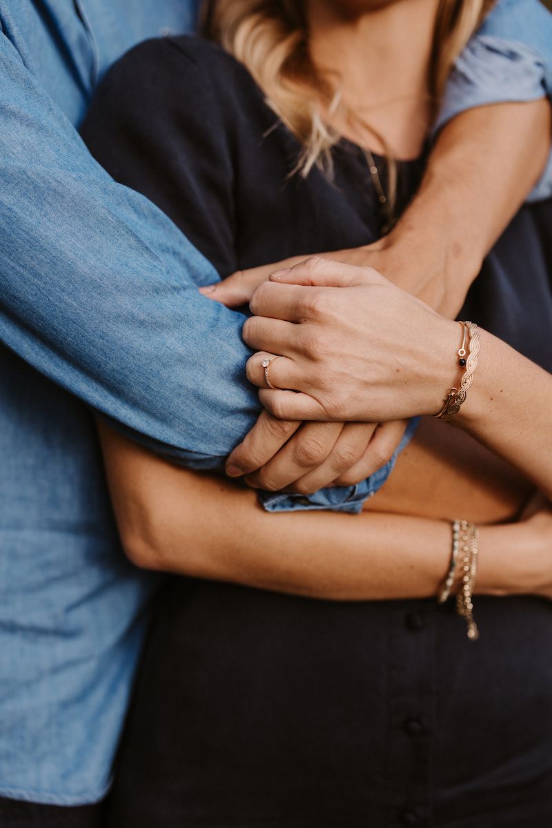 Close-up of hands embracing with jewelry and denim clothing details.