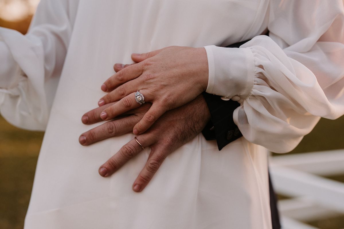 Wedding ring detail shot with flowing white fabric and gentle hands.