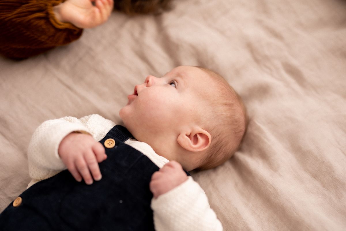 Close-up of a baby wearing a black and white outfit lying on beige bedding.