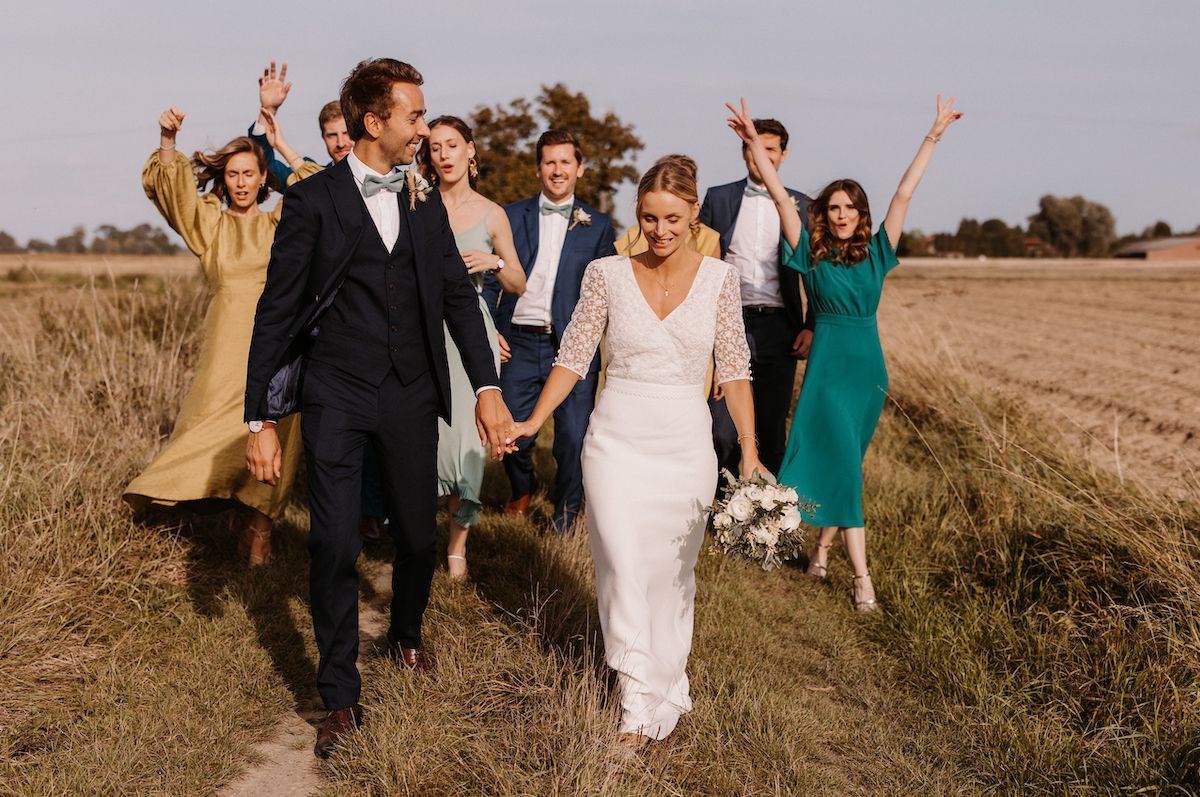 Wedding party celebrates joyfully while walking through an outdoor field setting.