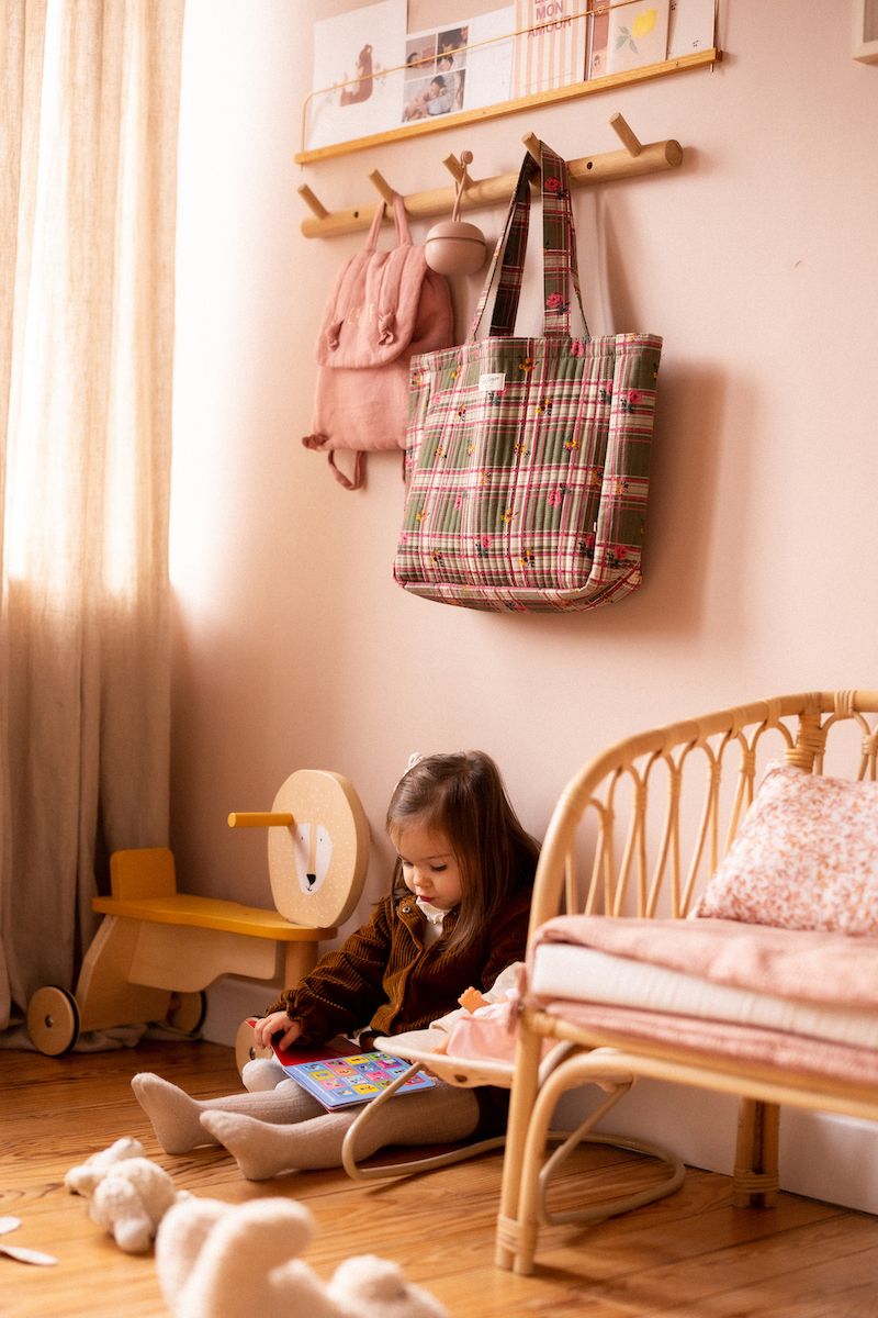 Cozy children's room with wooden furniture, plaid bags, and soft natural lighting.