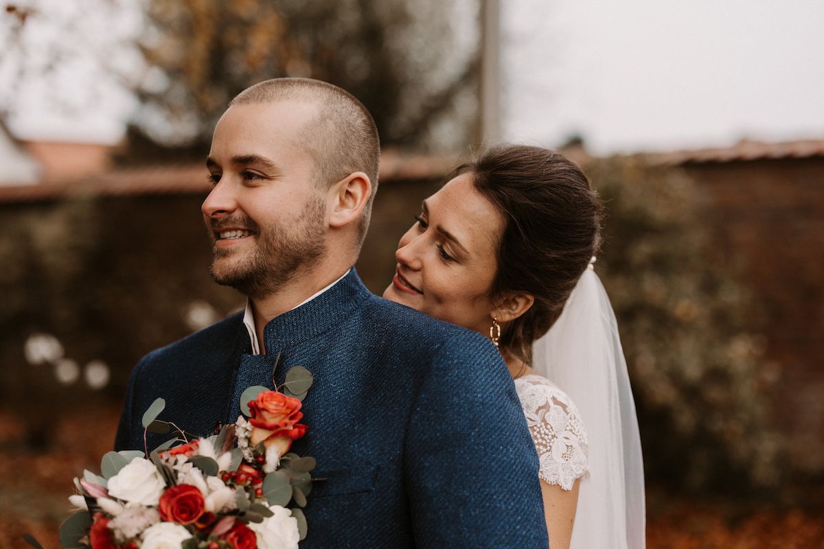 A joyful wedding portrait of a couple in navy and white lace sharing a candid moment with red floral bouquet.