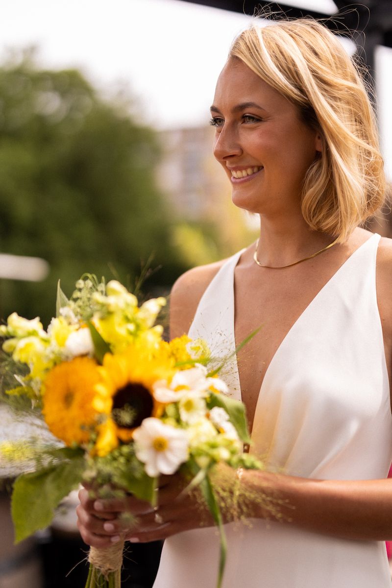 Bridesmaids in white dresses hold bright yellow sunflower bouquets during outdoor ceremony.