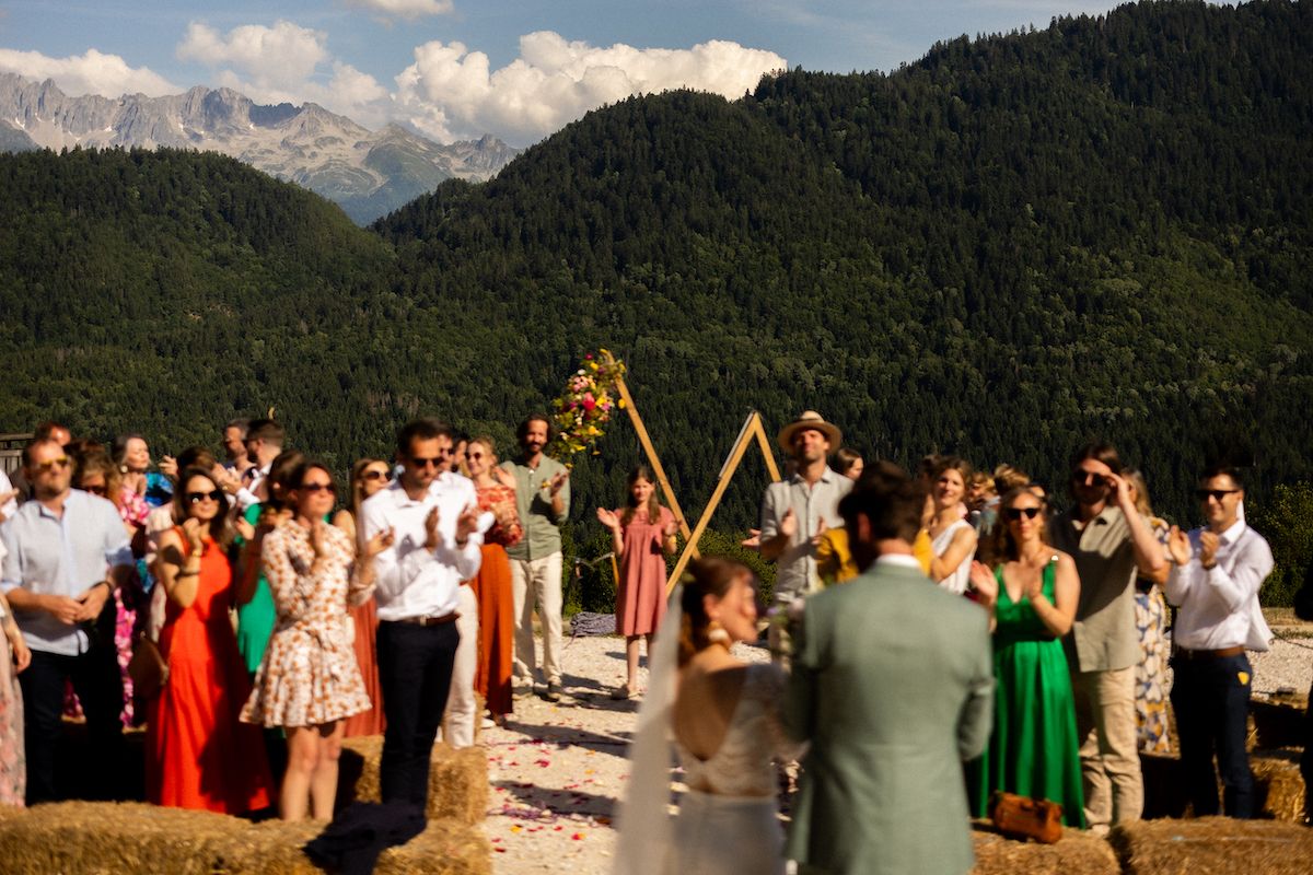 Scenic mountain wedding ceremony with wooden arch and gathered guests.